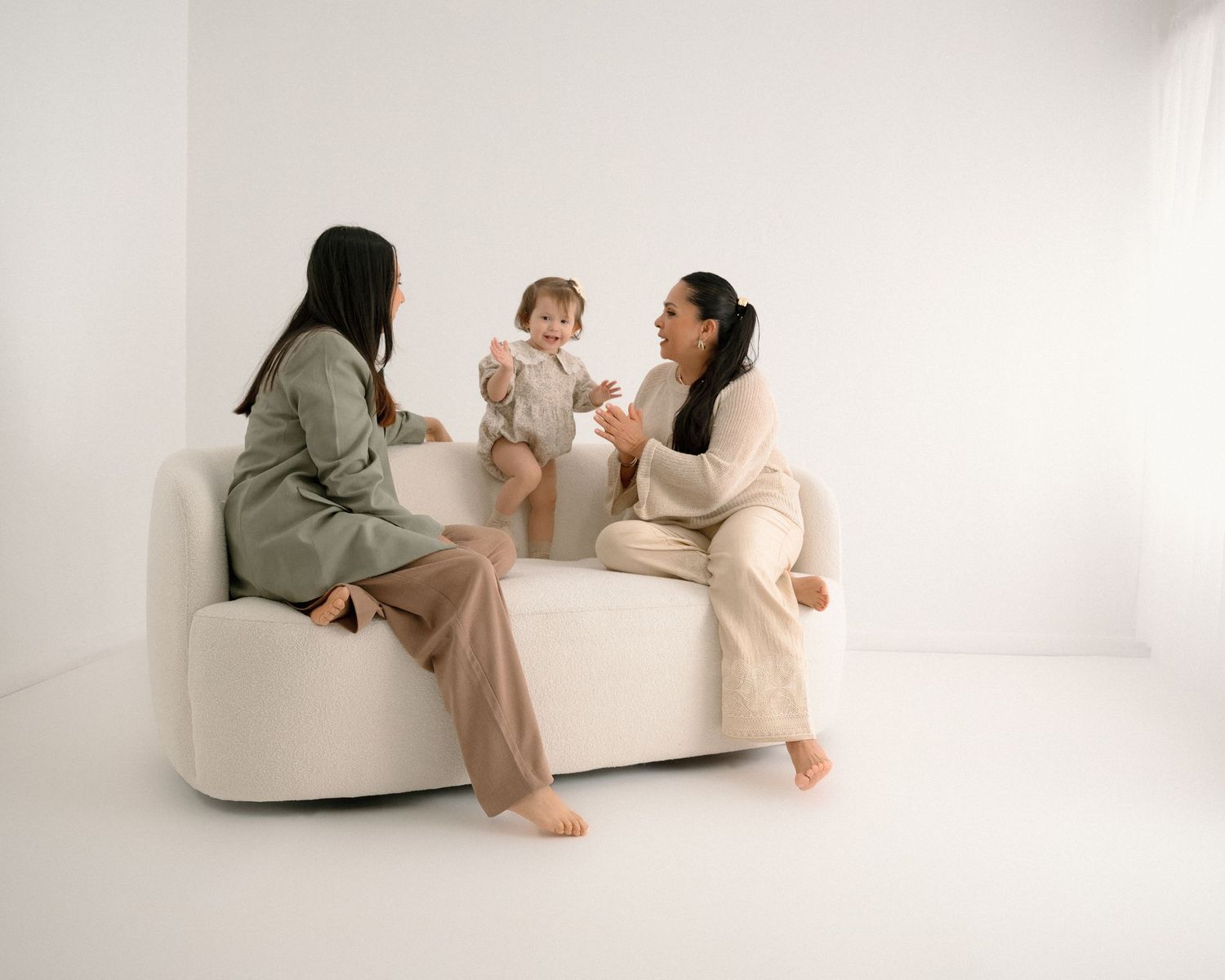 Family members in earth-toned clothing interact playfully on white studio floor.