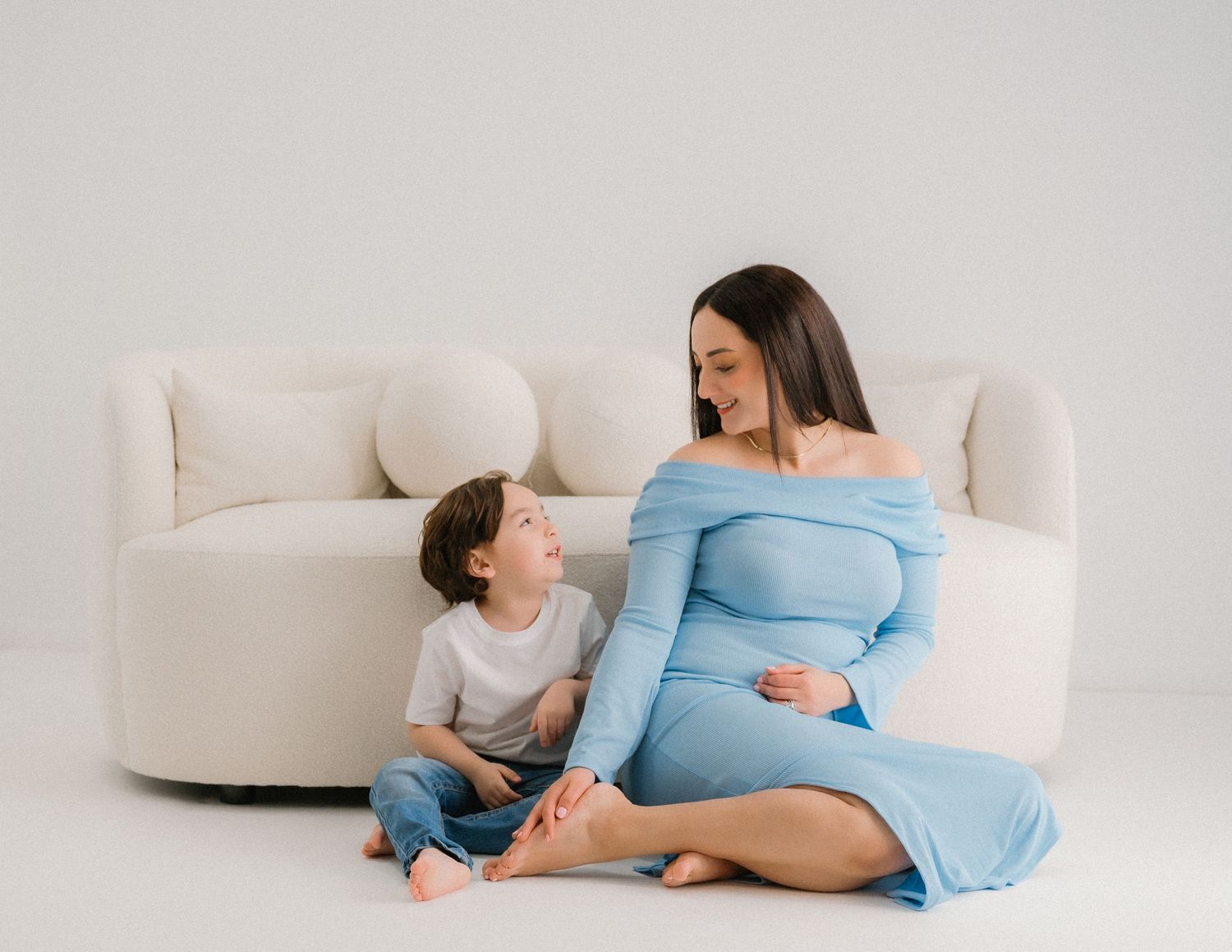 Mother and child in coordinated outfits lounging on white couch during maternity photoshoot.