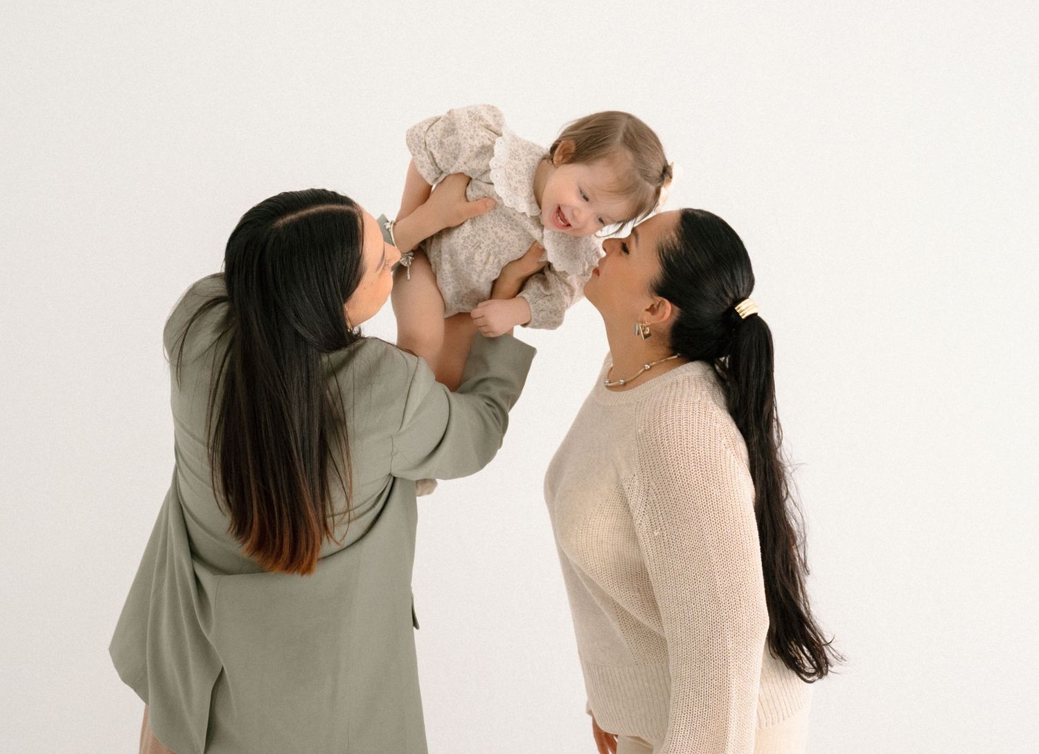 Artistic family photoshoot with parent and child playing against white backdrop.