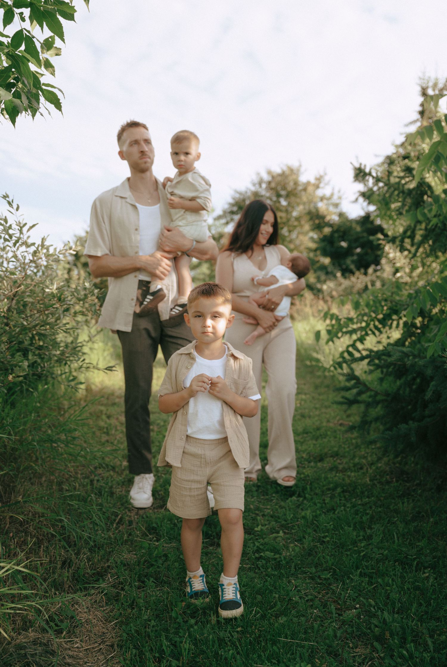 Family in coordinating neutral outfits explores a green outdoor setting.