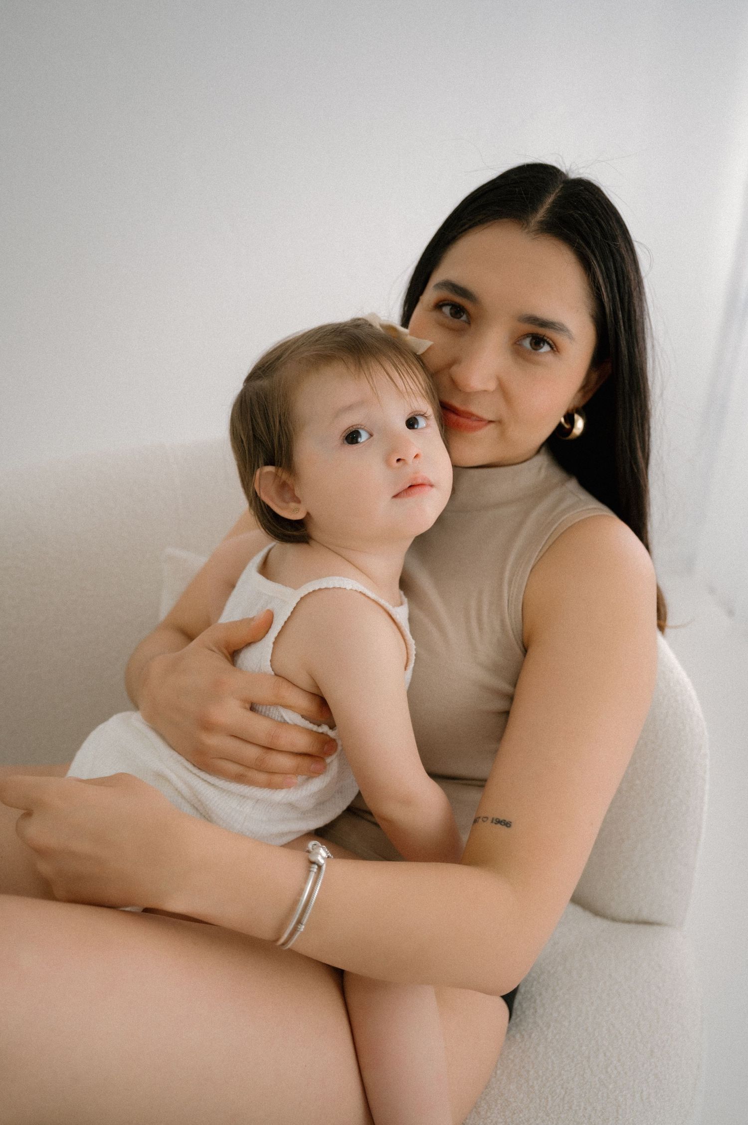 Intimate black and white portrait of parent and baby cuddling on white couch.