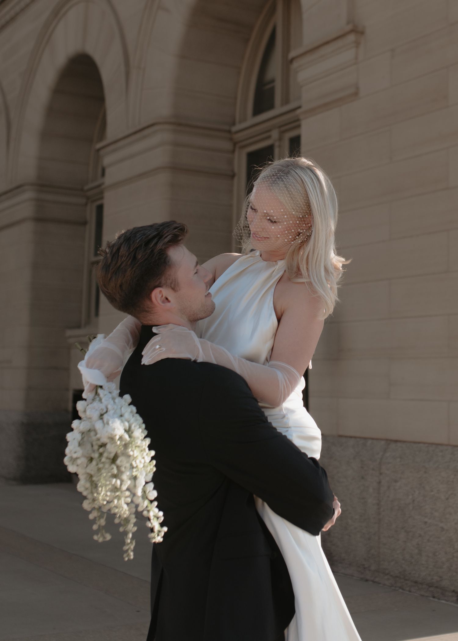 Romantic wedding dance captured against classic architectural backdrop with white floral bouquet.