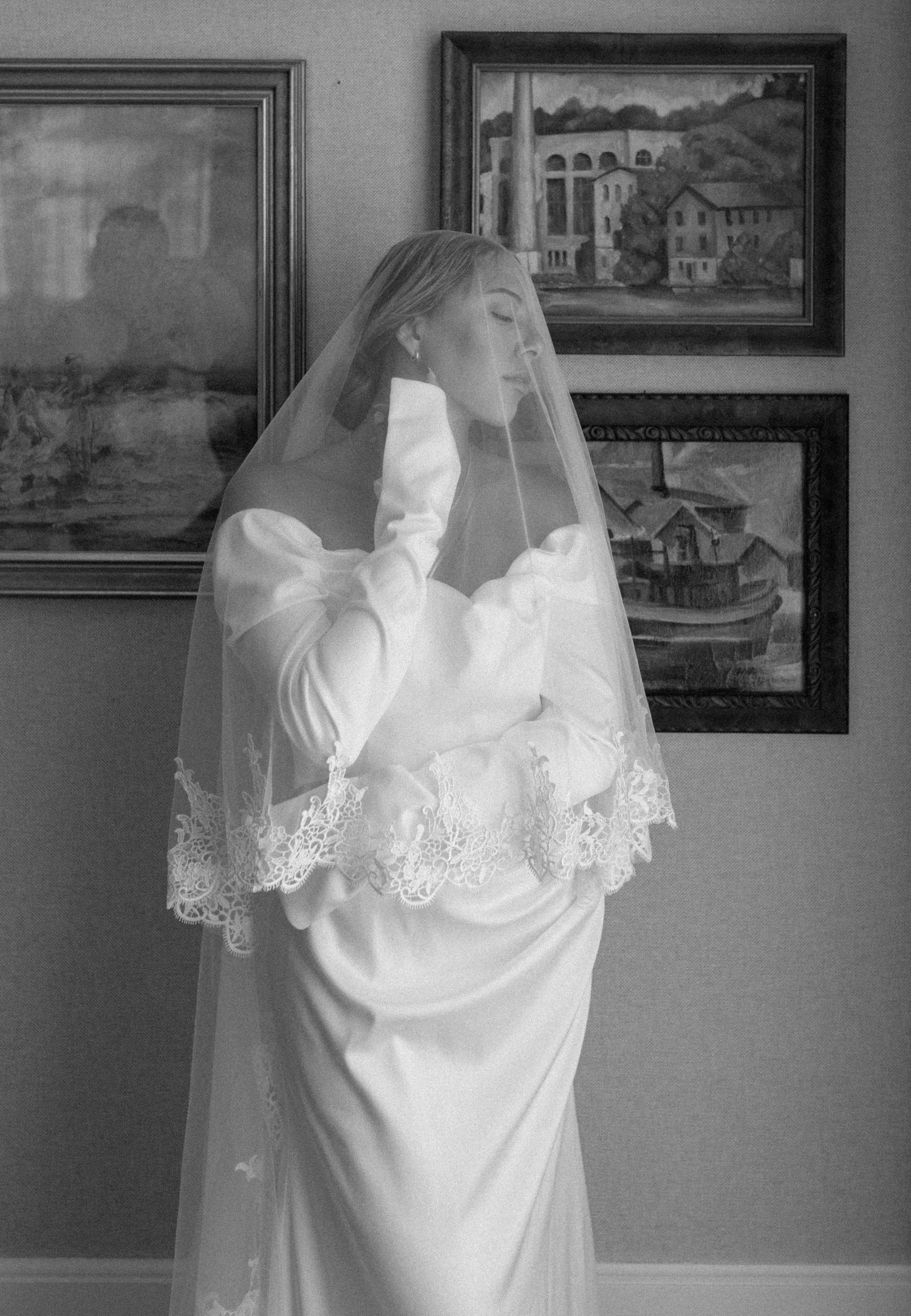 White wedding gown with lace details displayed against a wall of vintage framed artwork. Appleton, Green Bay & Kaukauna