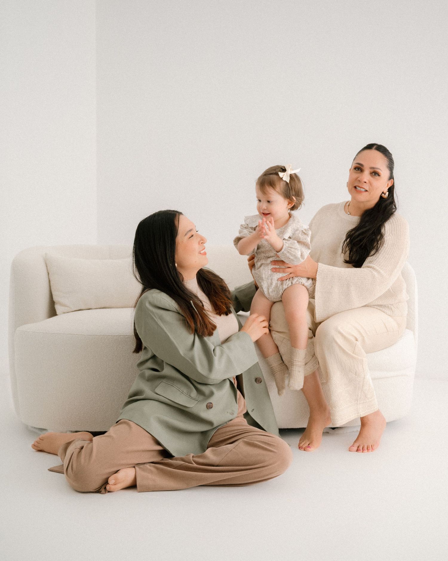 Family with baby relaxing together on white floor during indoor photoshoot.