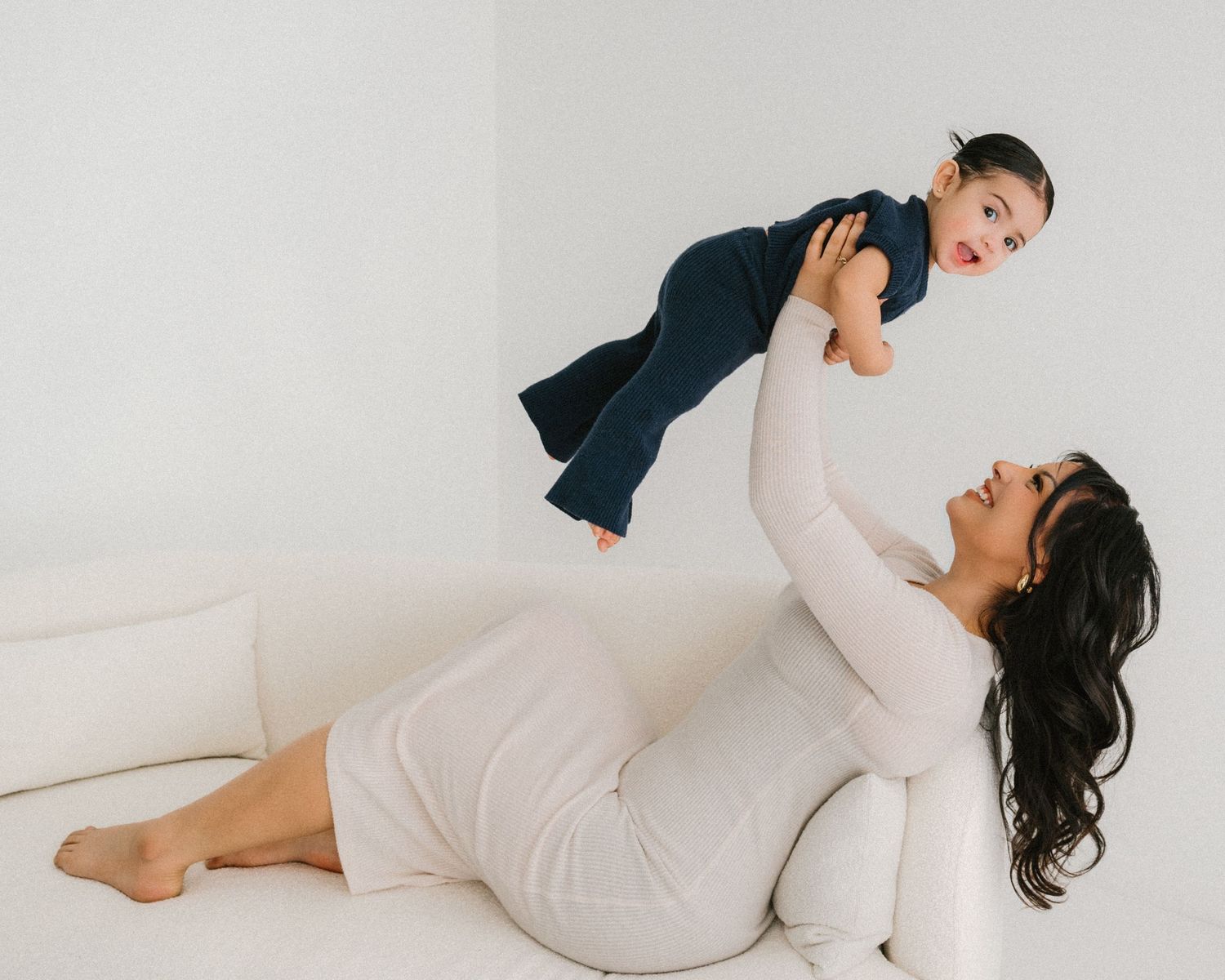 Family wearing contrasting white and navy outfits share intimate moments on a white couch.