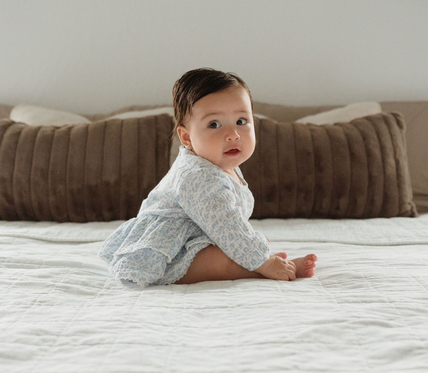 Baby crawling on white bedding wearing light blue outfit. Appleton, Green Bay & Kaukauna