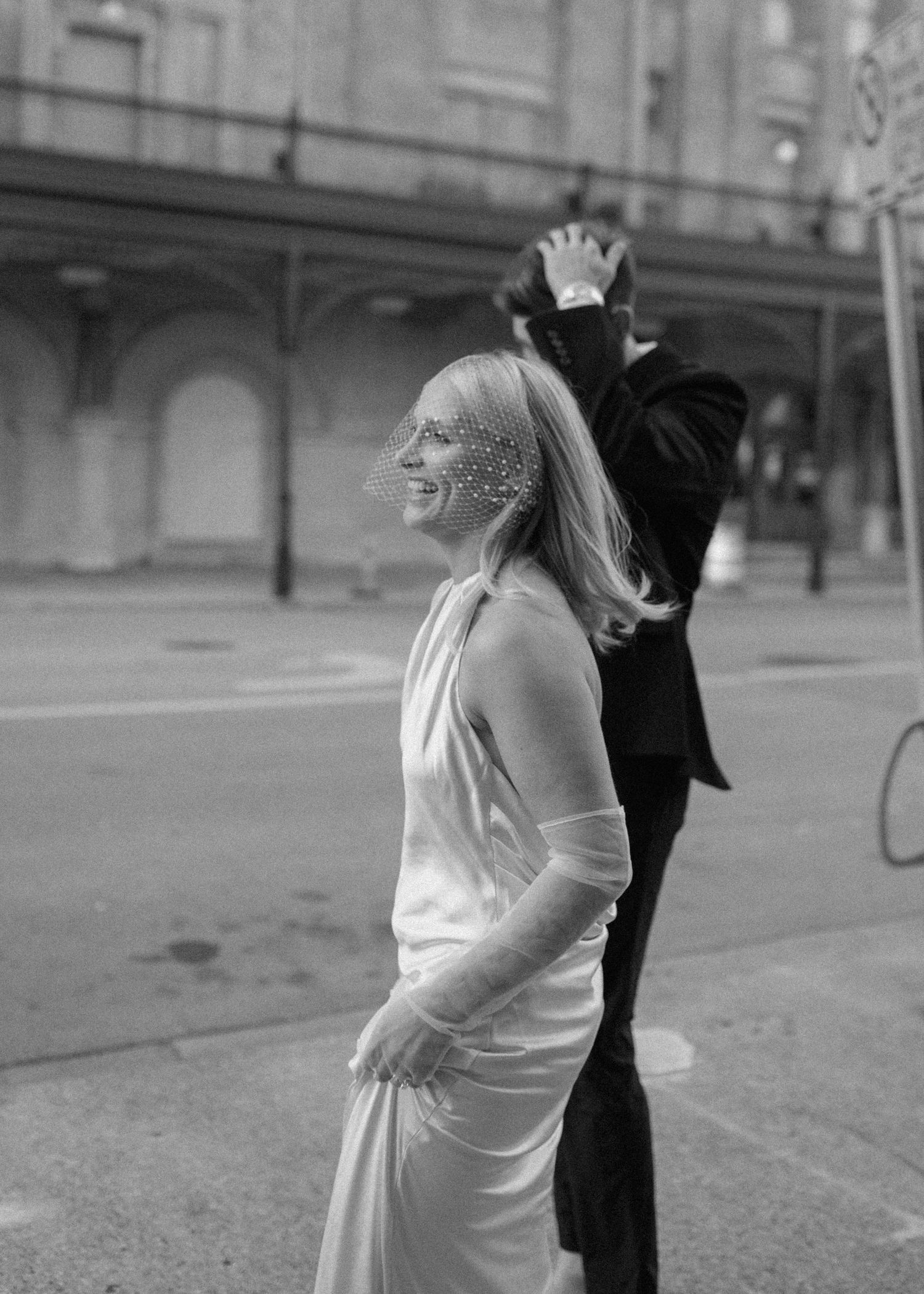Black and white photo capturing joyful moment between couple outside urban building.