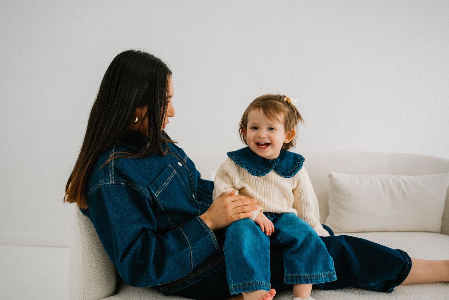 Playful interaction between parent in navy outfit and child on white couch.