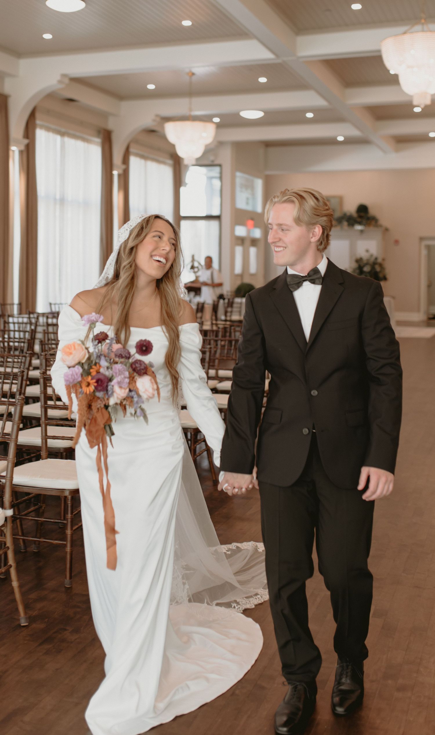 A couple laughing together in a spacious wedding venue with hardwood floors and elegant decor.
