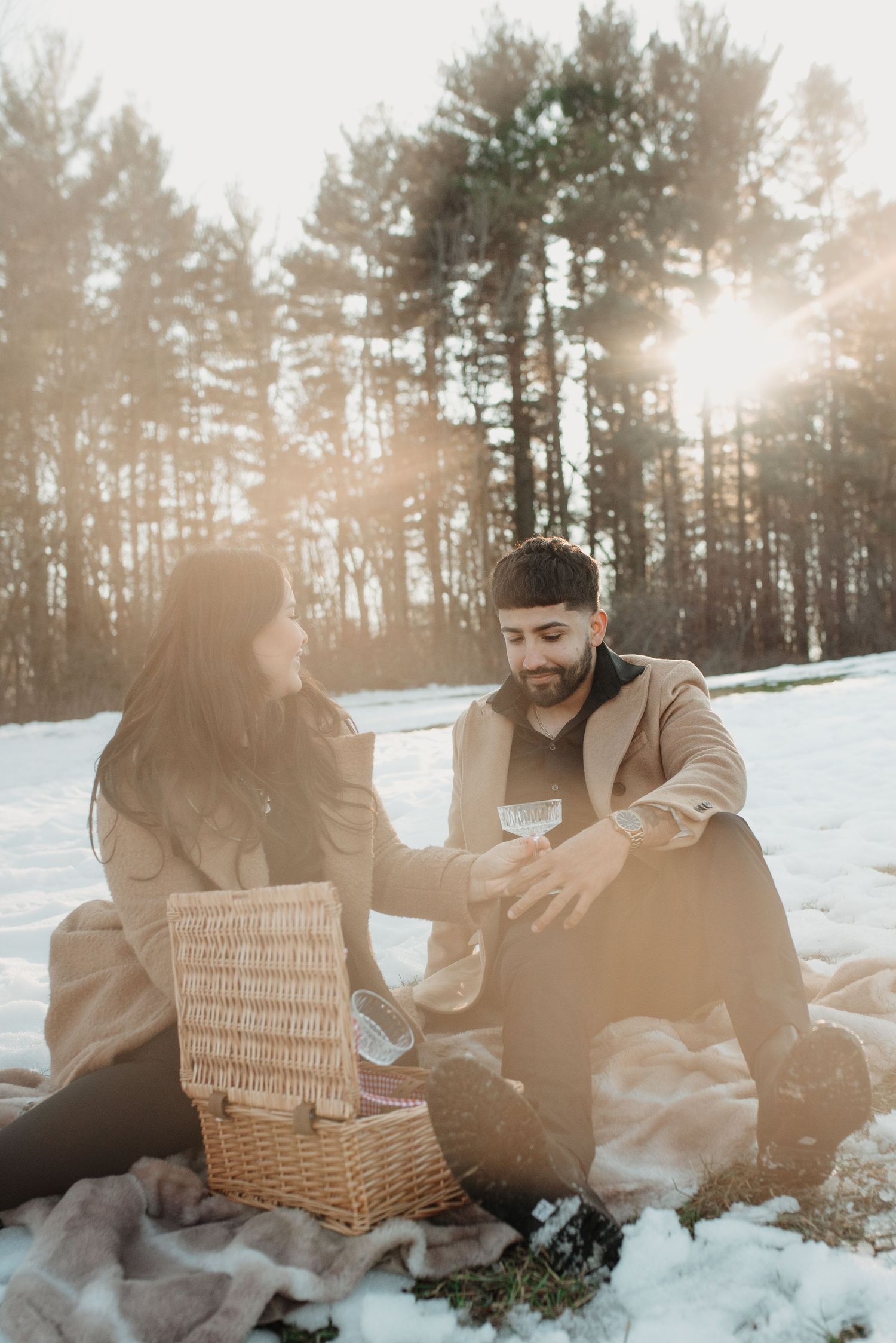 A winter picnic scene in a snowy forest with a wicker basket during golden hour sunset.