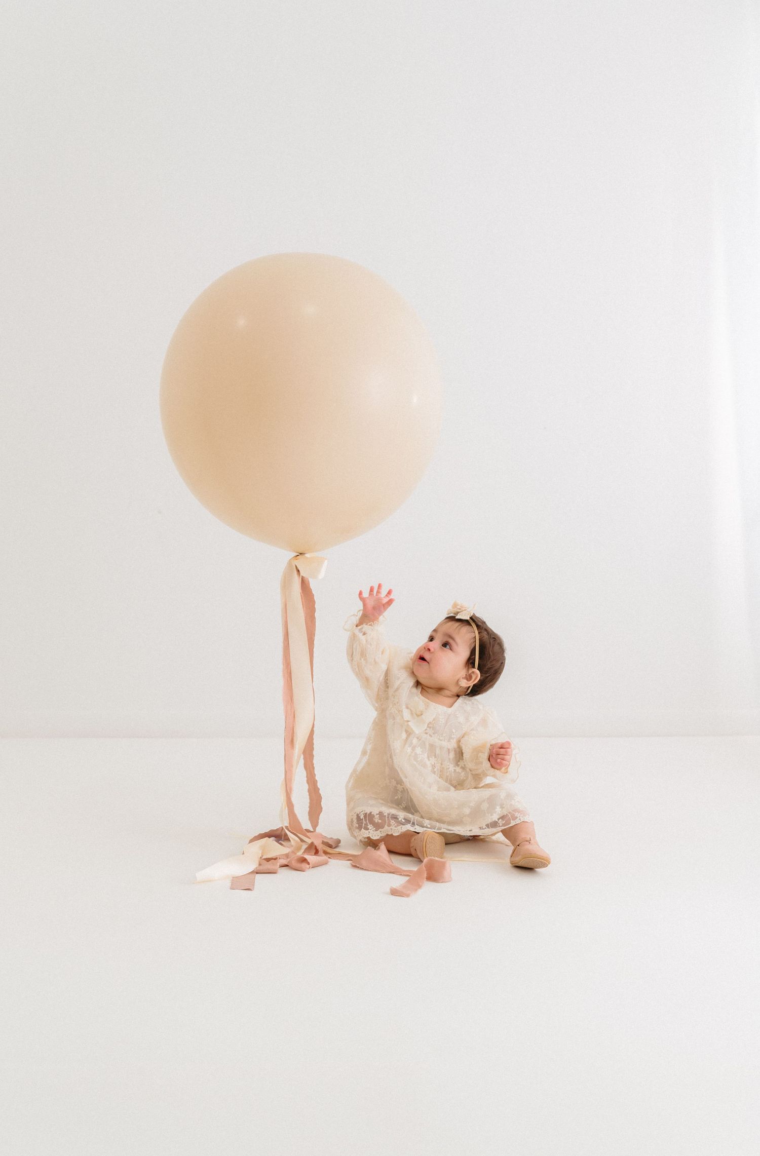 Baby playing with large peach balloon on white studio floor. Appleton, Green Bay & Kaukauna