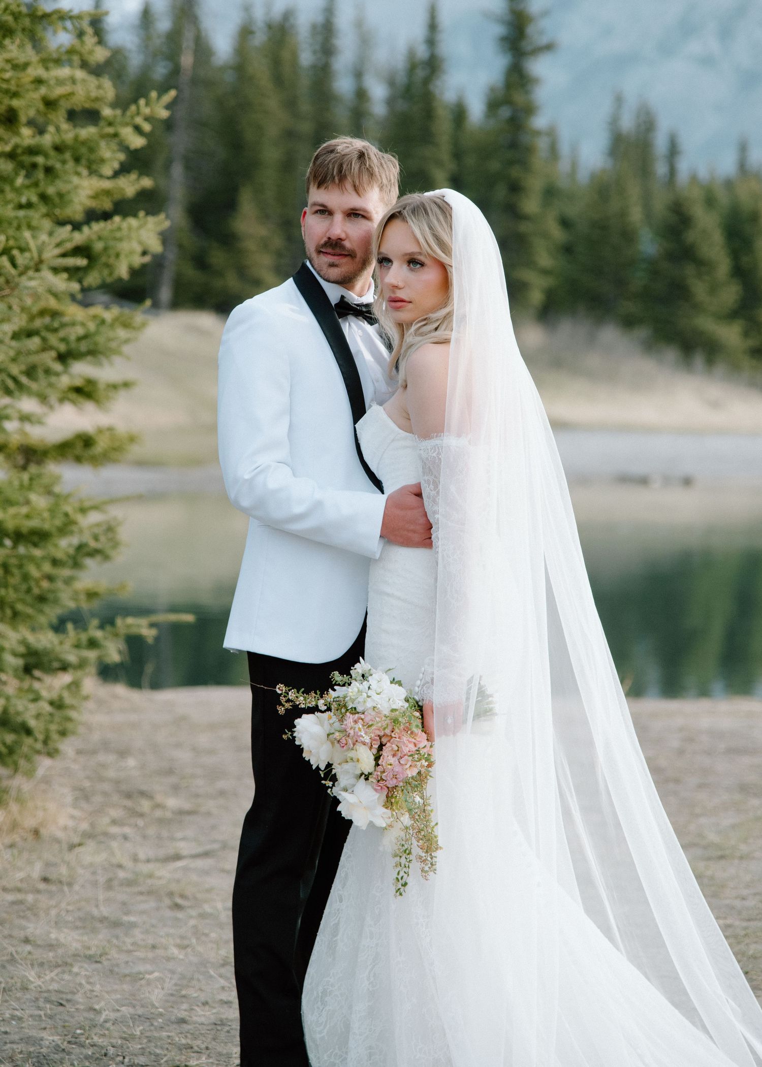 Elegant wedding portraits by a mountain lake with white floral bouquet details. Banff and Calgary Wedding Photographer