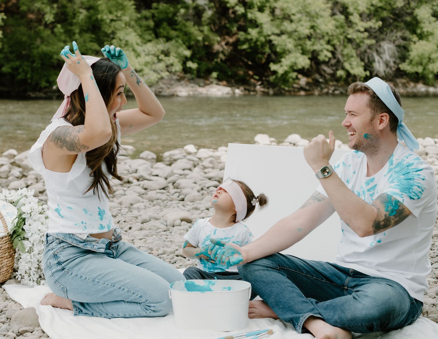 A family wearing blindfolds plays with paint while sitting on a blanket outdoors. Calgary Alberta Family and Maternity Photographer.