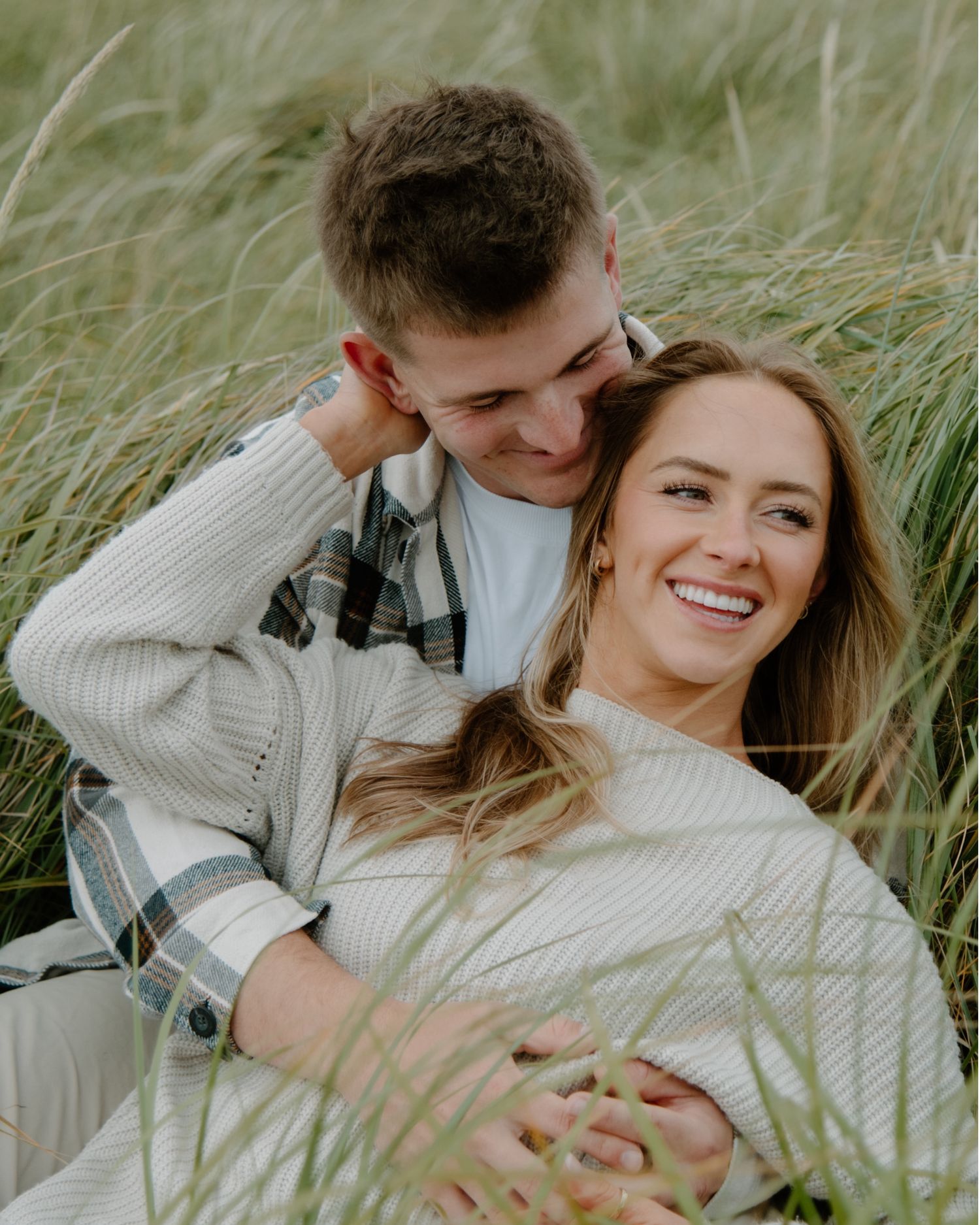 Couple relaxes together in tall grass field during golden hour on Oregon Coast. Calgary Alberta Lifestyle and Engagement Photographer.