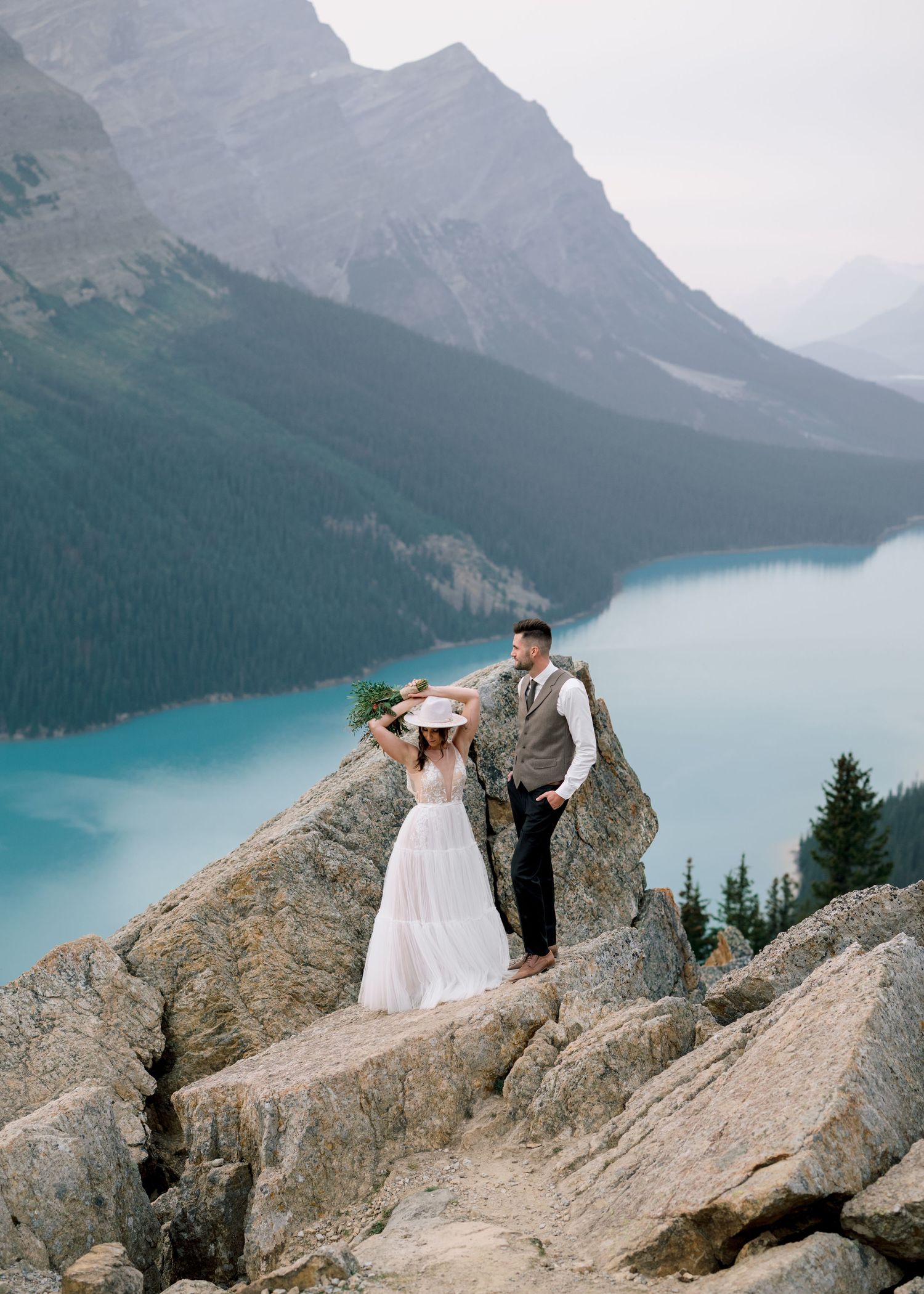A couple poses on rocky cliffs overlooking the stunning turquoise waters of Peyto Lake in Banff National Park.