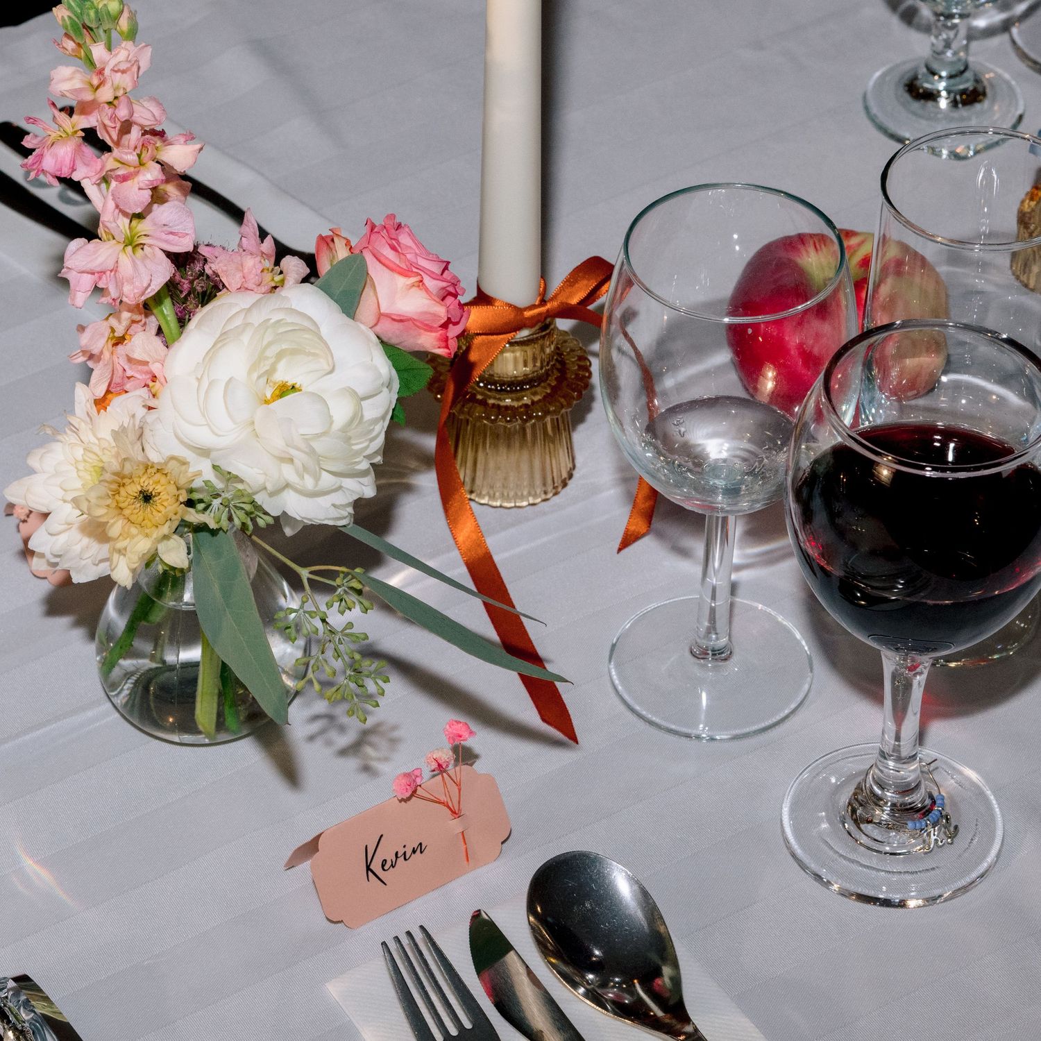 Multiple wine glasses on a table with rose flower centerpieces and place cards set for a formal dining event.