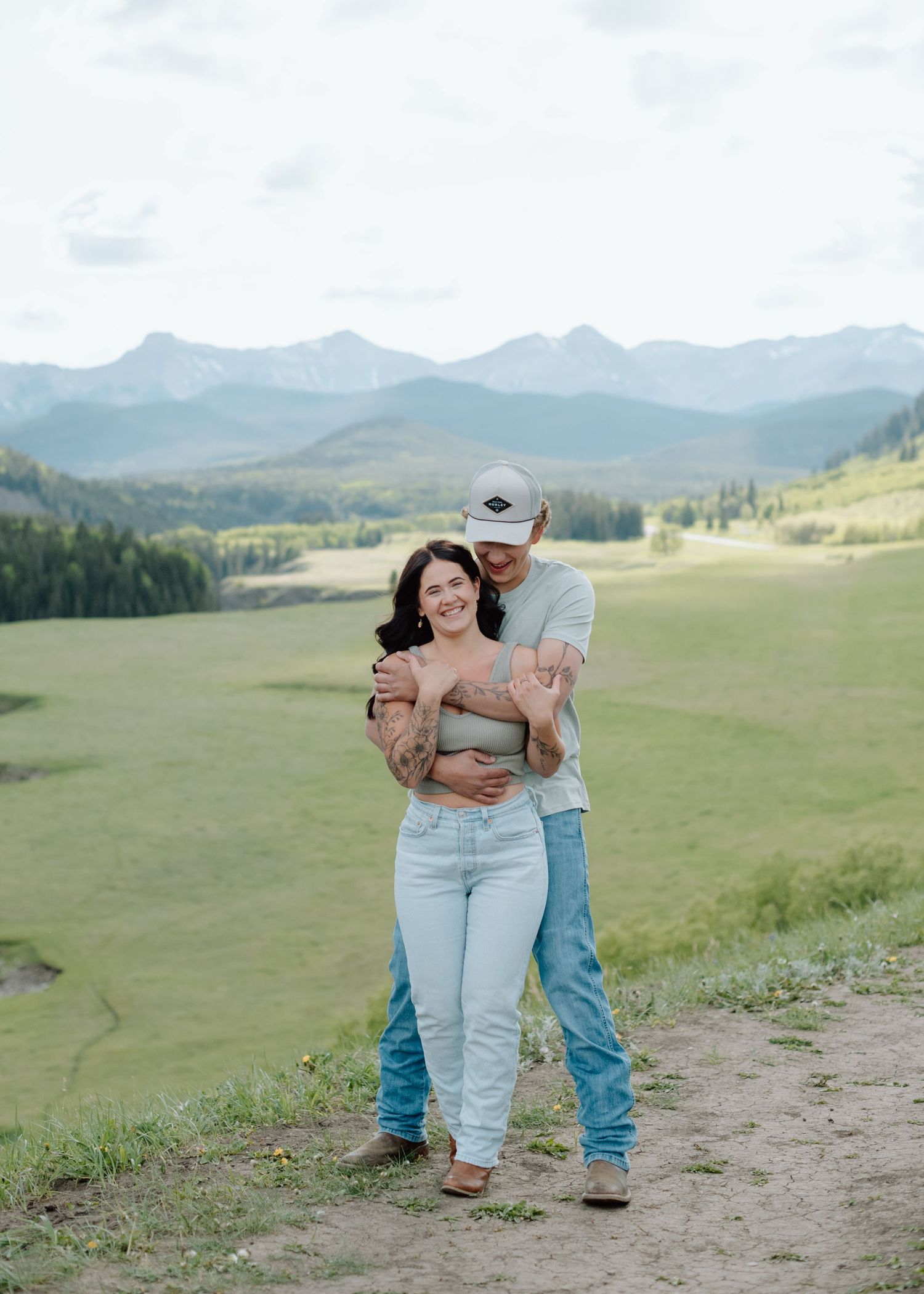 Two people embracing on a hilltop with dramatic mountain views in the background. Calgary Alberta Engagement Photographer.