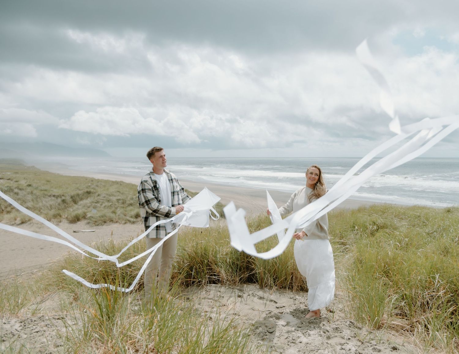 A couple plays with billowing white fabric on a scenic coastal dune on Oregon Coast. Calgary Lifestyle and Engagement Photographer.