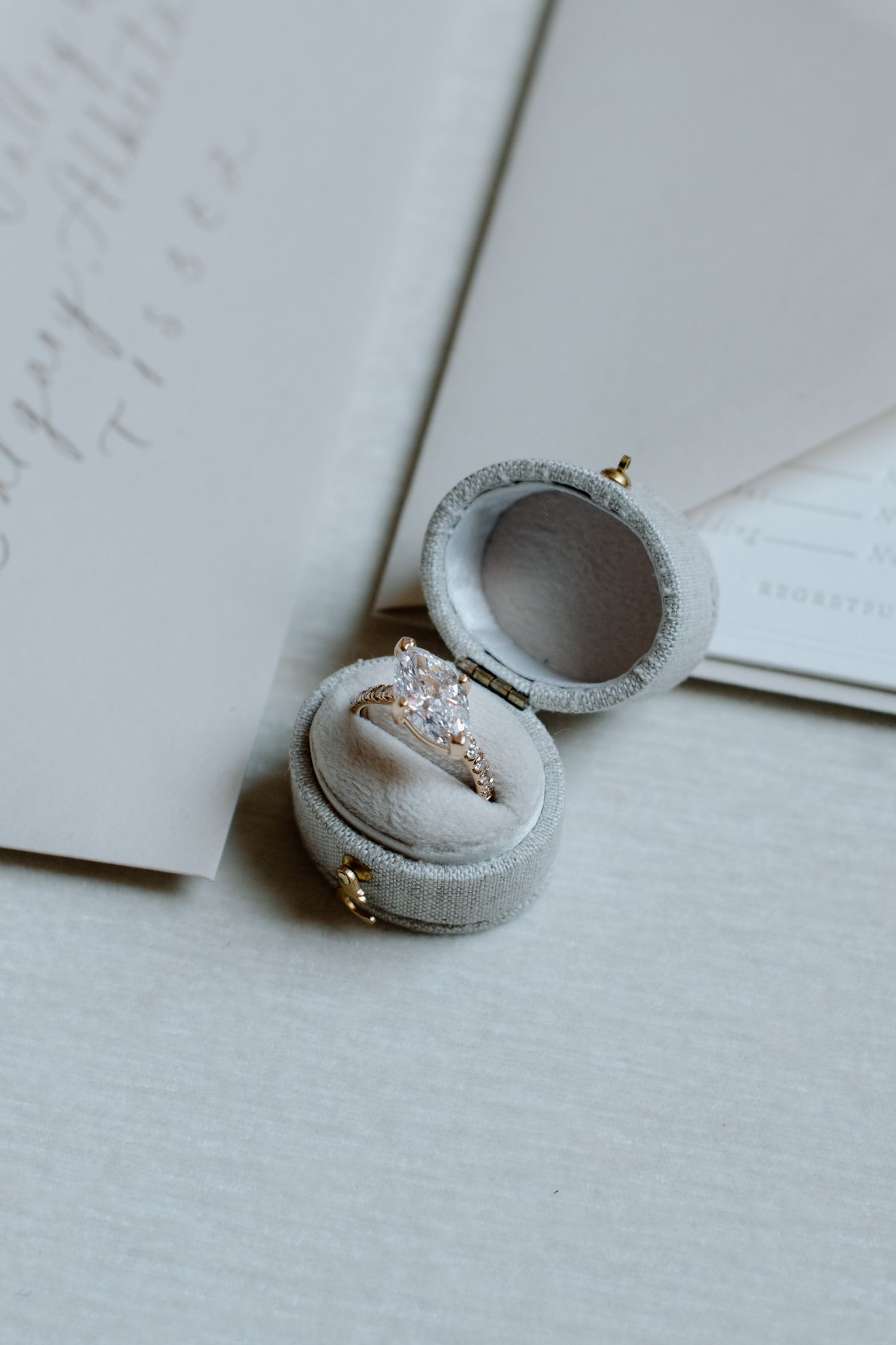 A sparkly engagement ring sits in a light grey velvet ring box on white paper at the Brownstone YYC. Calgary Wedding Photographer