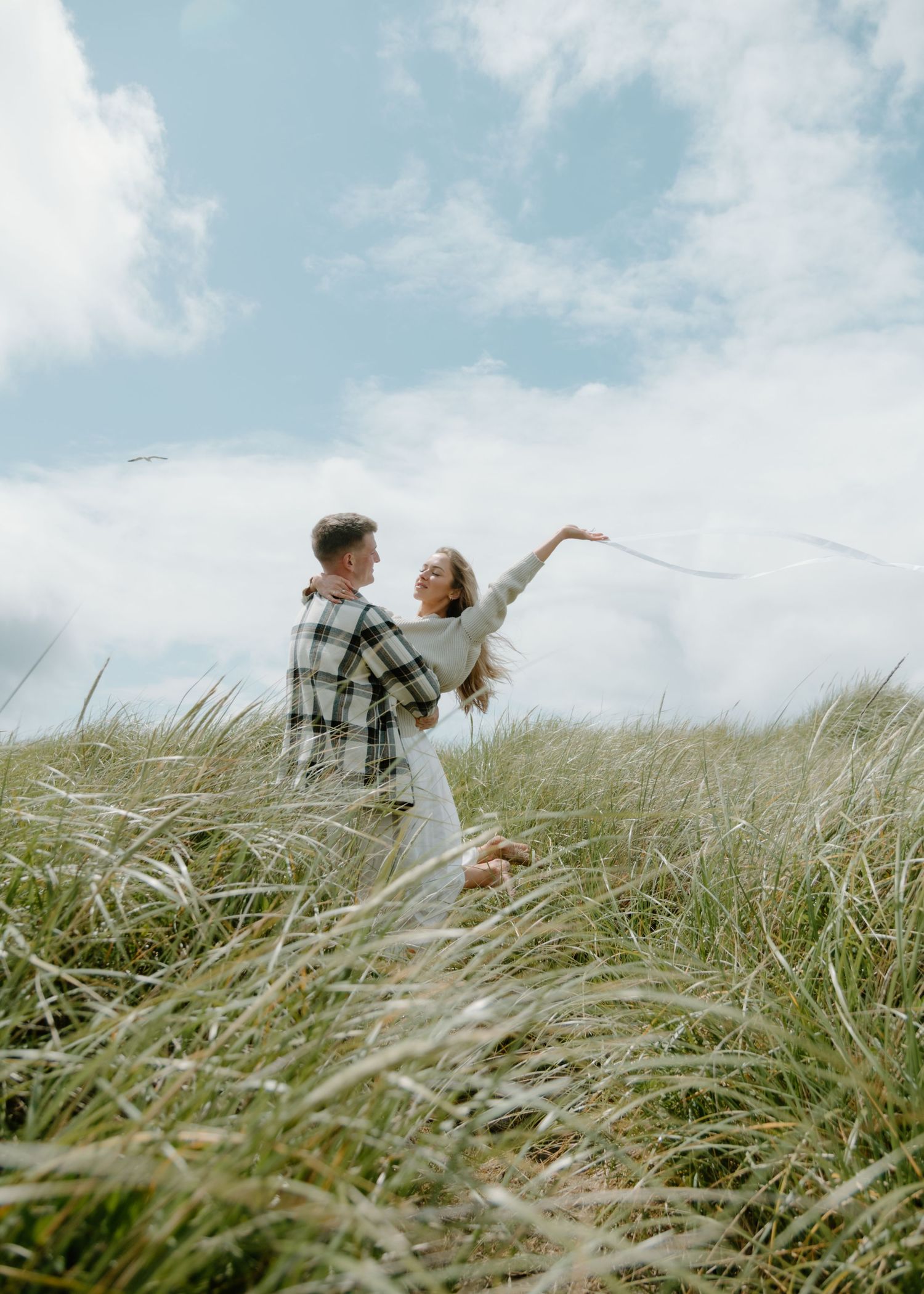 A joyful dance in tall coastal grass under blue skies on Oregon Coast. Calgary Lifestyle and Engagement Photographer.