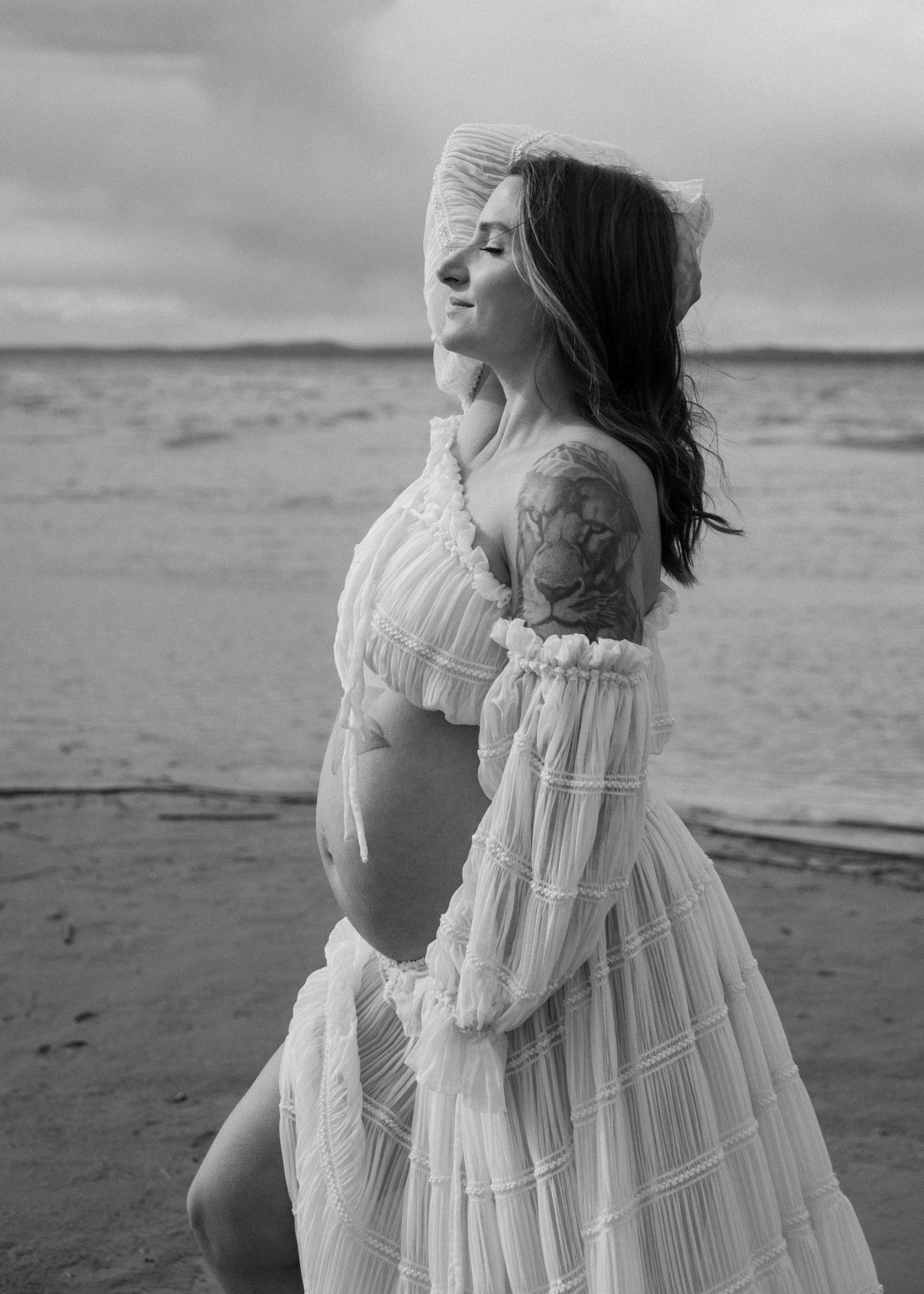 A black and white maternity photo showing a flowing white dress on a moody beach landscape. Calgary Alberta Maternity Photographer.