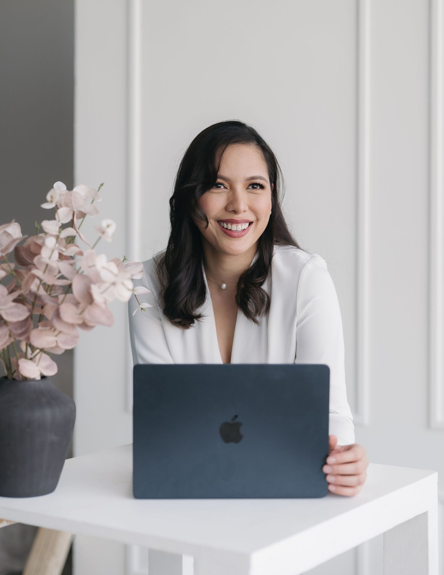 Professional working at desk with laptop and pink flowers in modern minimalist workspace setting.