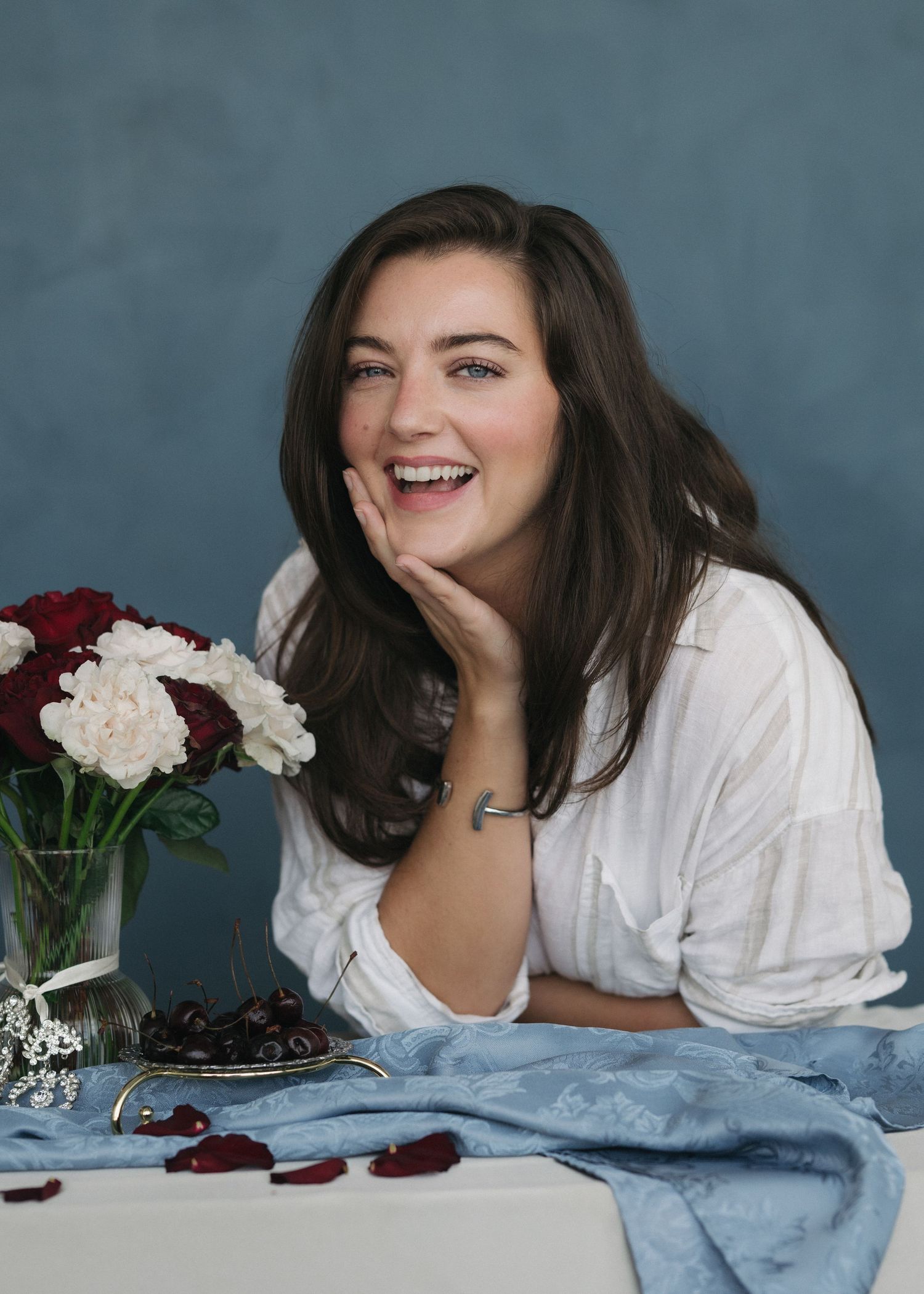 A person in a white shirt poses playfully on blue fabric with red and white roses in a creative photo series.
