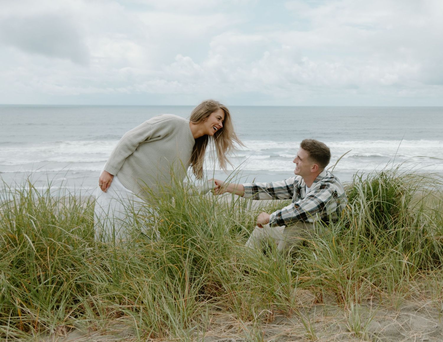 Couple sharing tender moment while sitting in coastal dunes by the ocean on Oregon Coast. Calgary Lifestyle and Engagement Photographer.