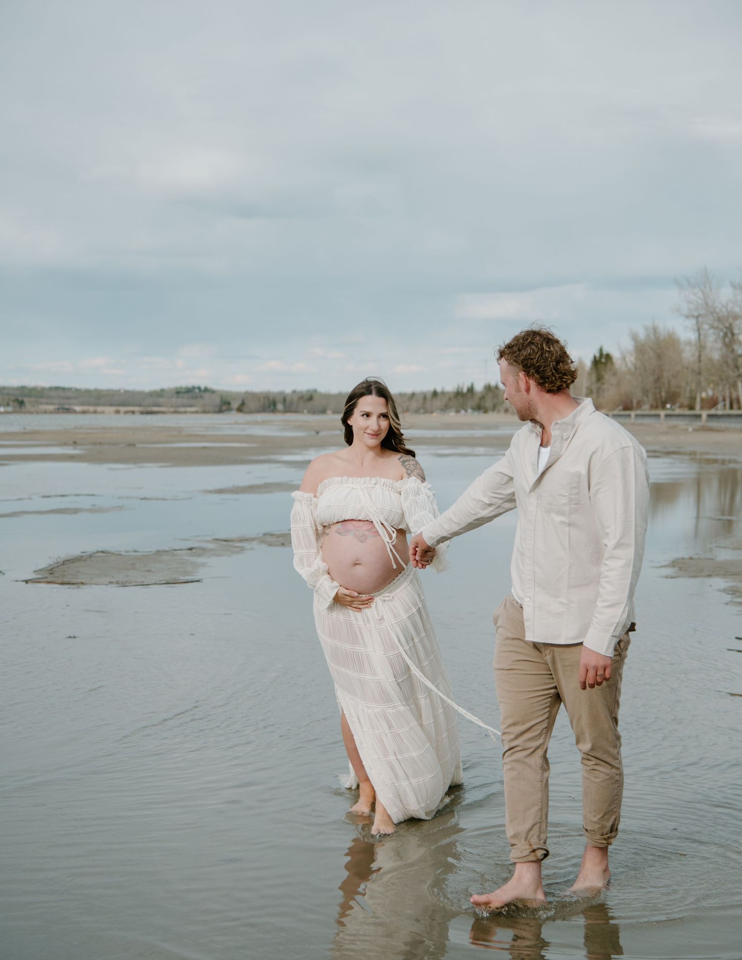 Gentle moment captured during a beachside maternity session in flowing white dress. Calgary Alberta Maternity Photographer.