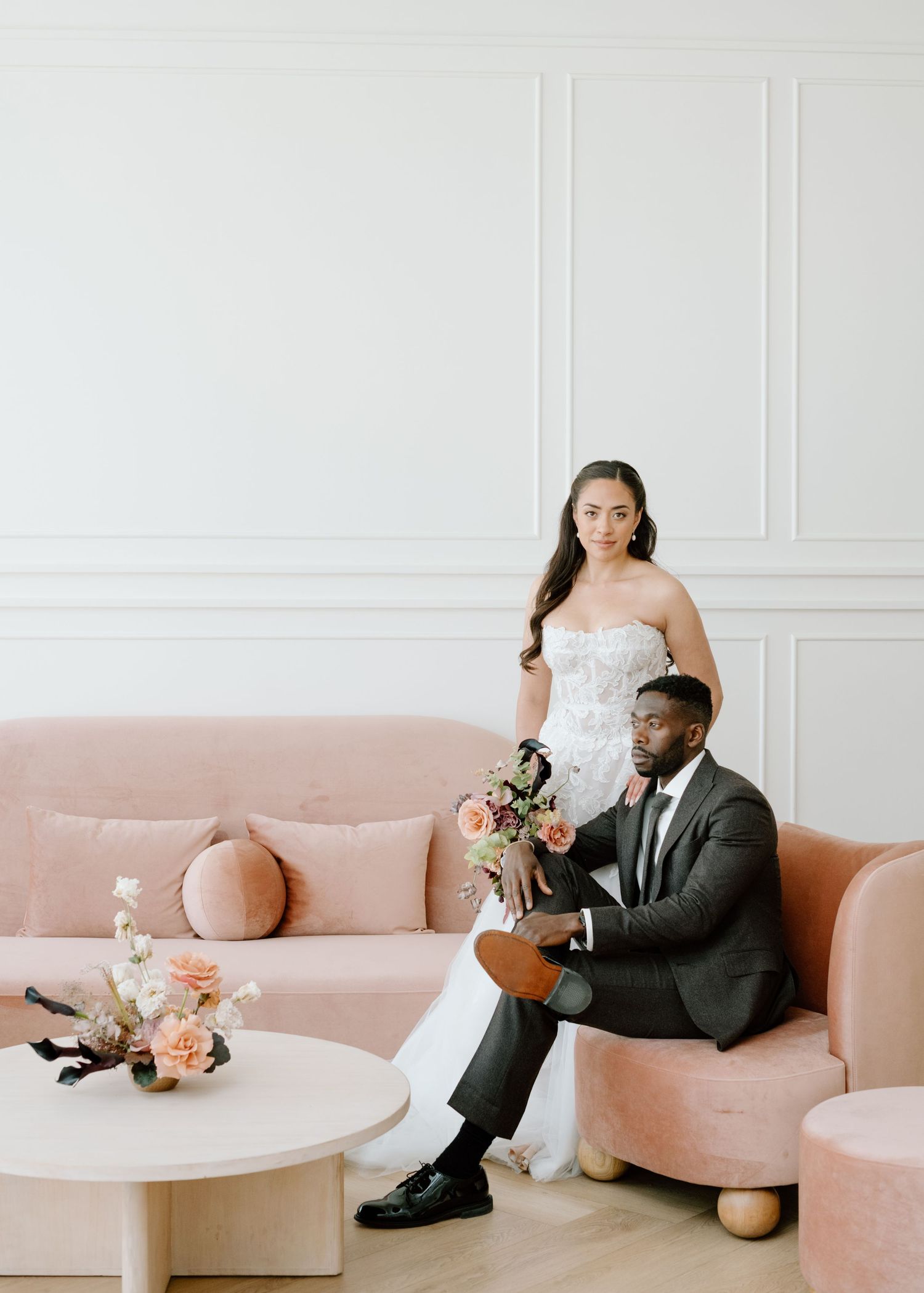 A wedding couple poses on a pink sofa in an elegant white room with modern decor at the Studio at Vic Park YYC Wedding Photographer