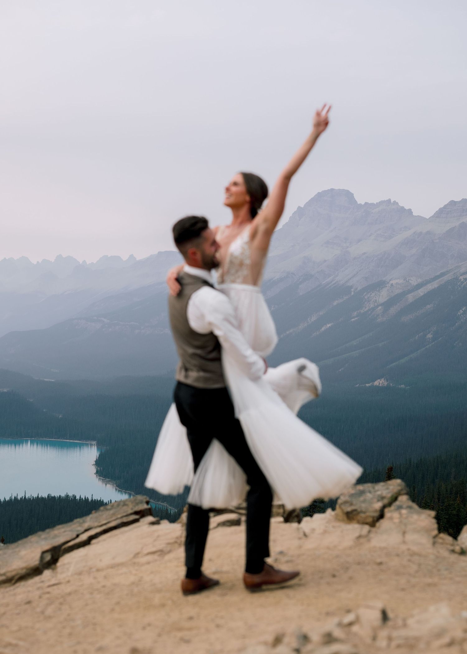 A couple performs playful dance poses against a stunning mountain backdrop overlooking Peyto Lake in Banff National Park.