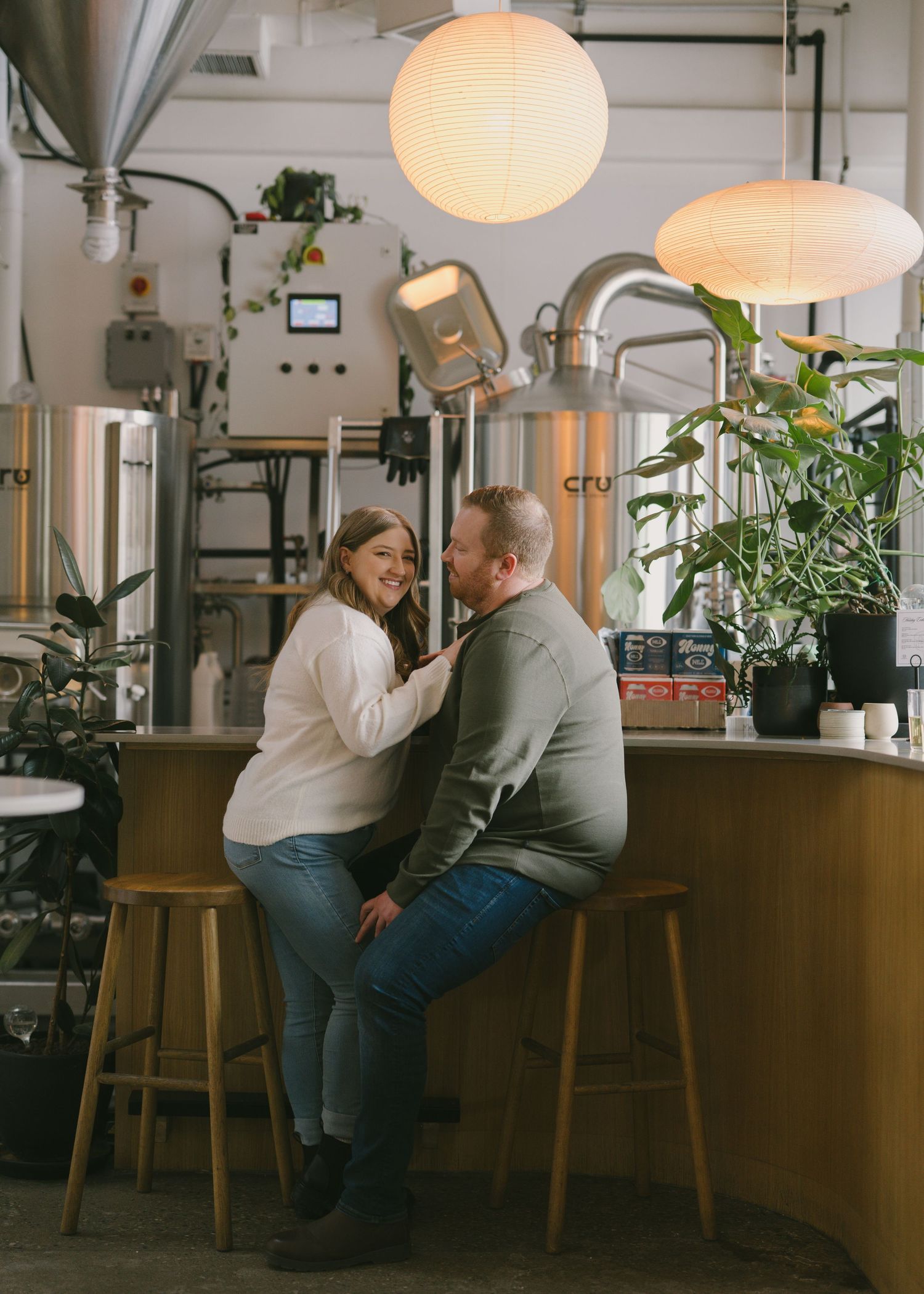 A cozy coffee shop interior with round paper lantern lights, wooden barstools, and brewing equipment in the background.