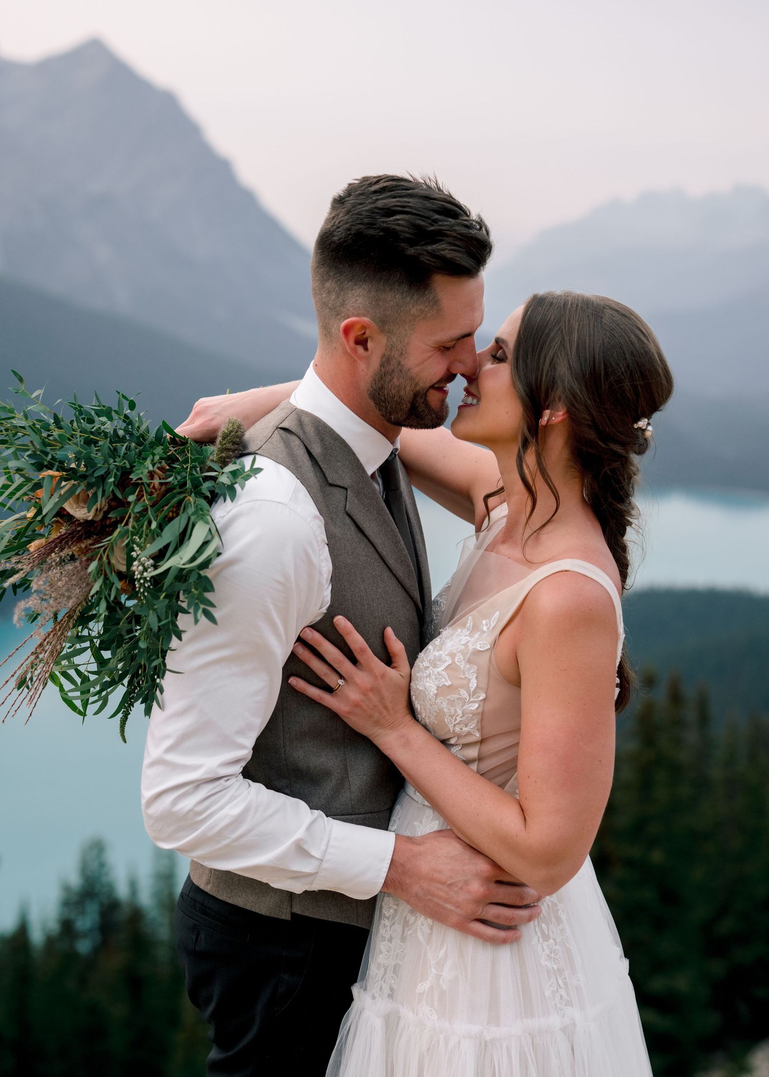 A romantic embrace between newlyweds with a scenic mountain lake backdrop at sunset.