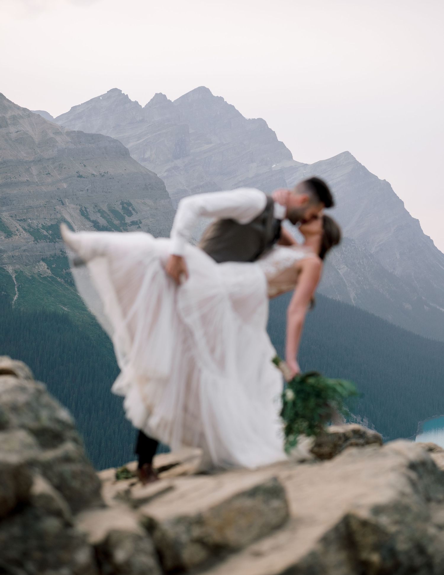 A white wedding dress creates an ethereal silhouette against rugged mountain scenery in soft focus.