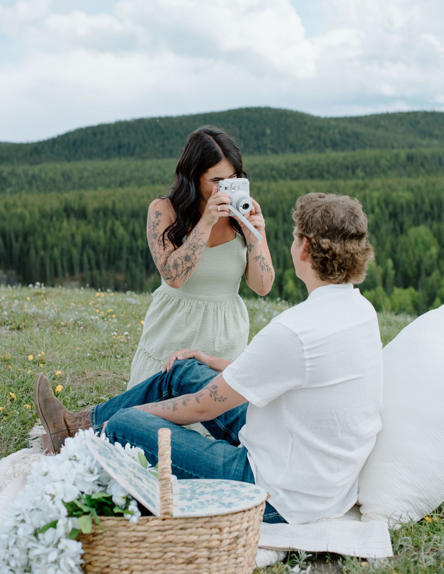 Couple enjoying romantic picnic on hillside meadow overlooking forest landscape. Calgary engagement photographer