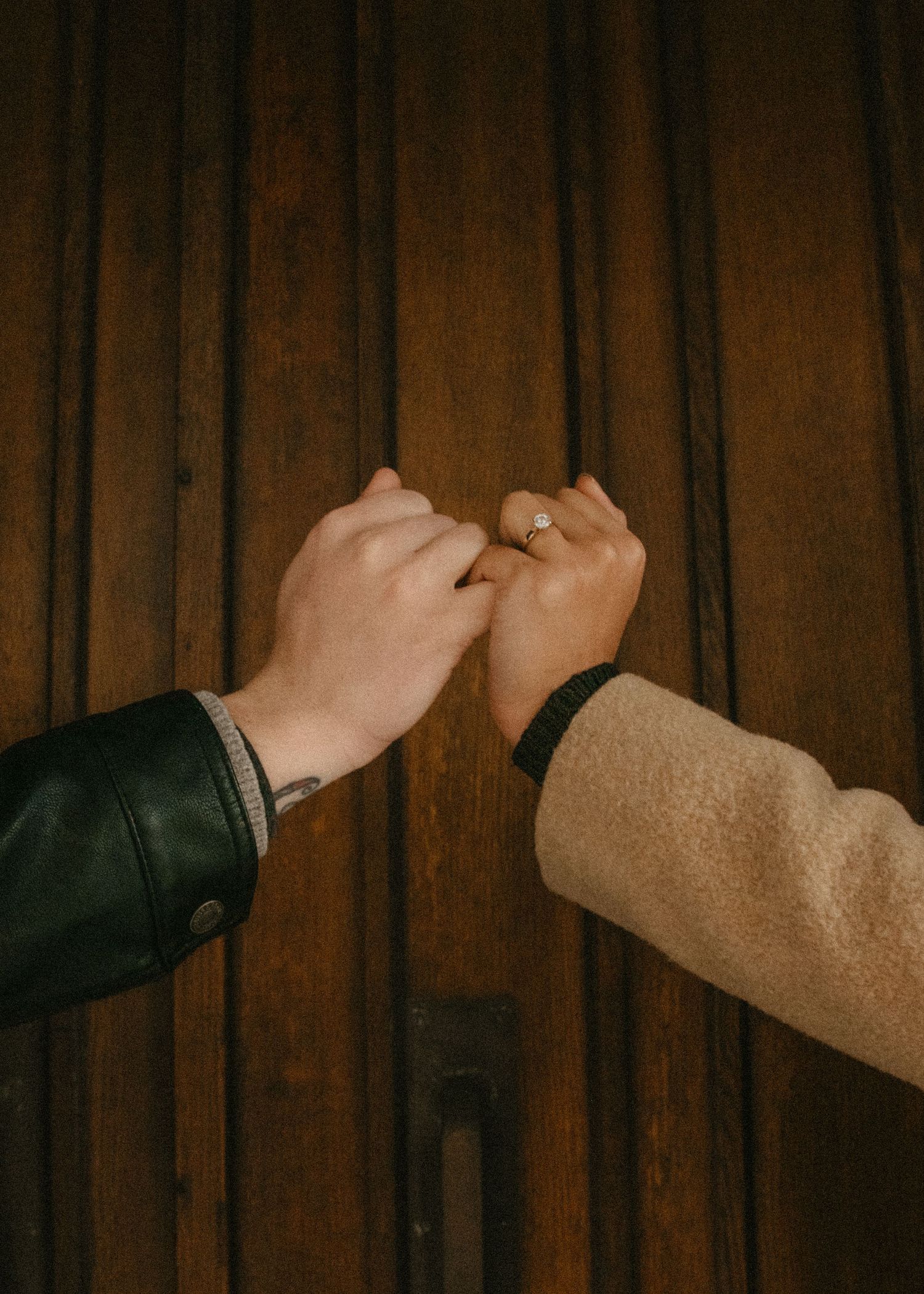Close-up of hands against dark wooden paneling showing sequential gestures in dim lighting. Calgary Alberta Engagement Photographer.