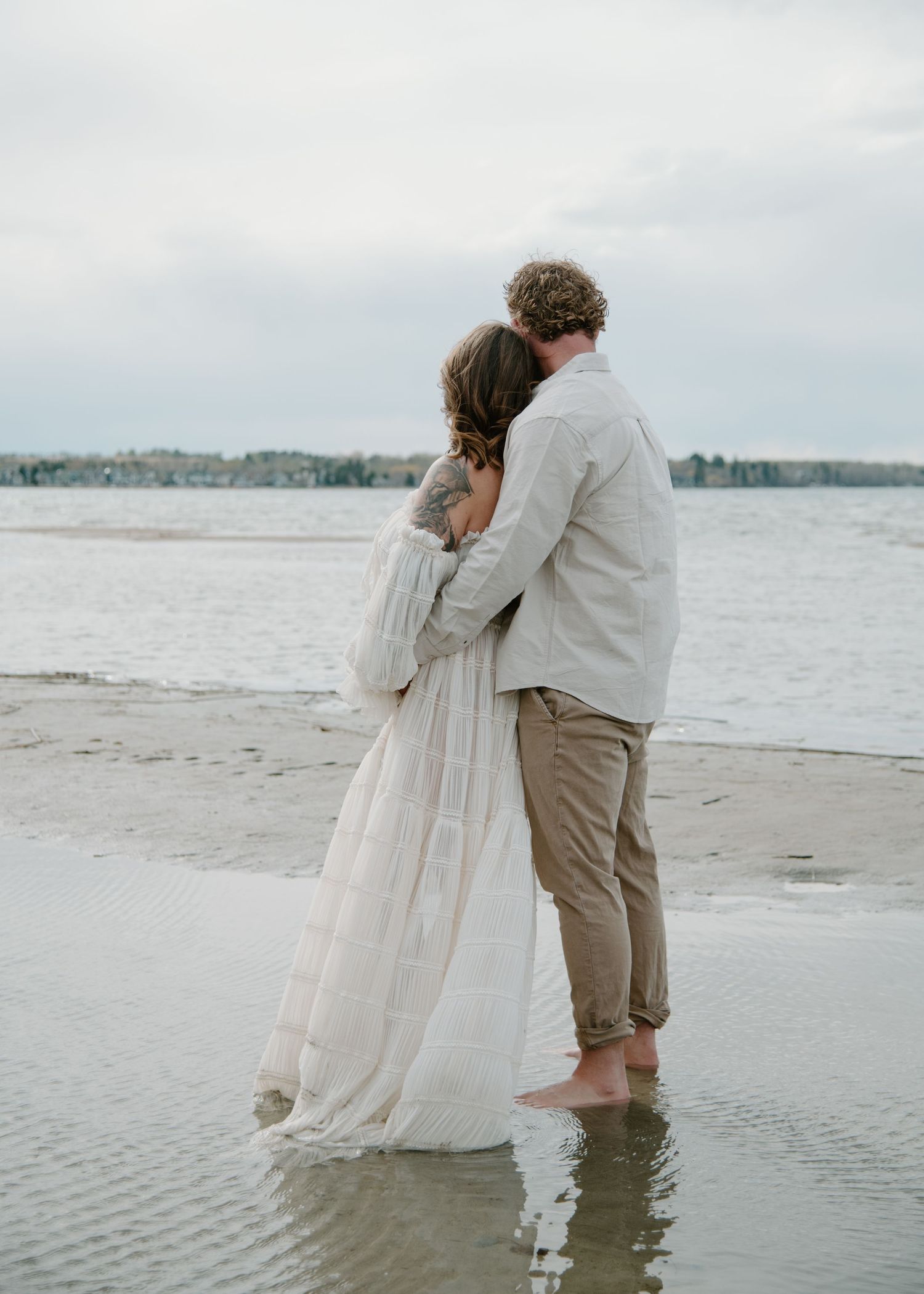 Romantic couple standing in shallow water during beach maternity photo session. Calgary Alberta Maternity Photographer.