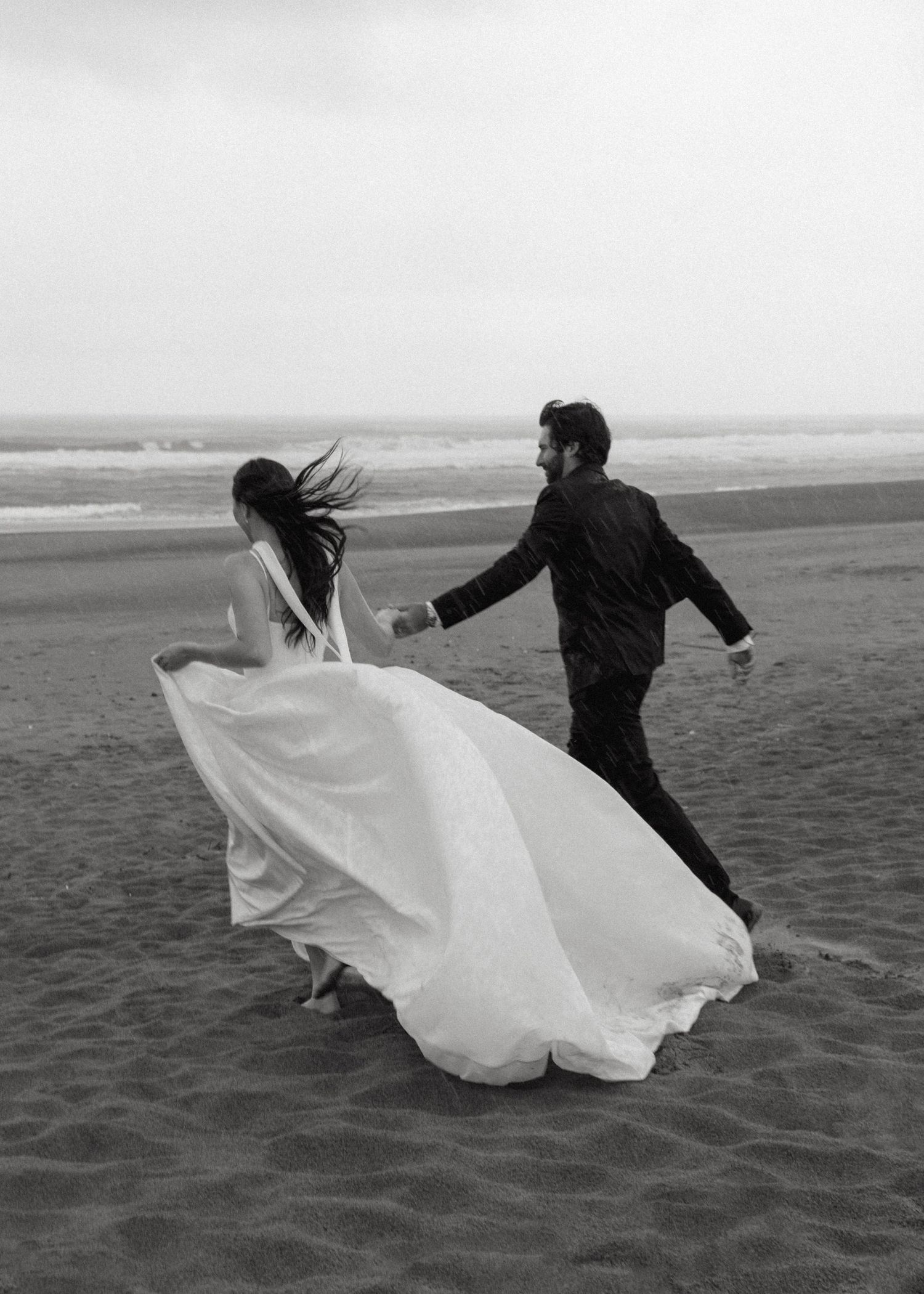 A romantic black and white sequence of a couple running and dancing together on a windswept beach with flowing fabrics.