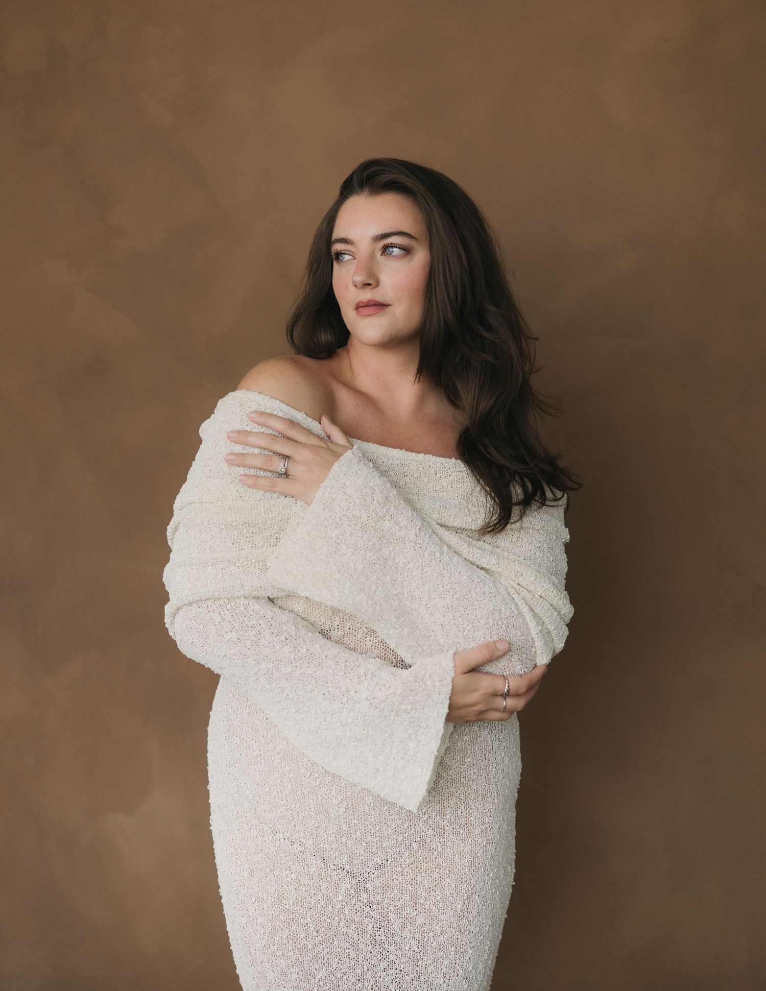 Woman in a textured white sweater poses against brown backdrop in artistic portrait series.