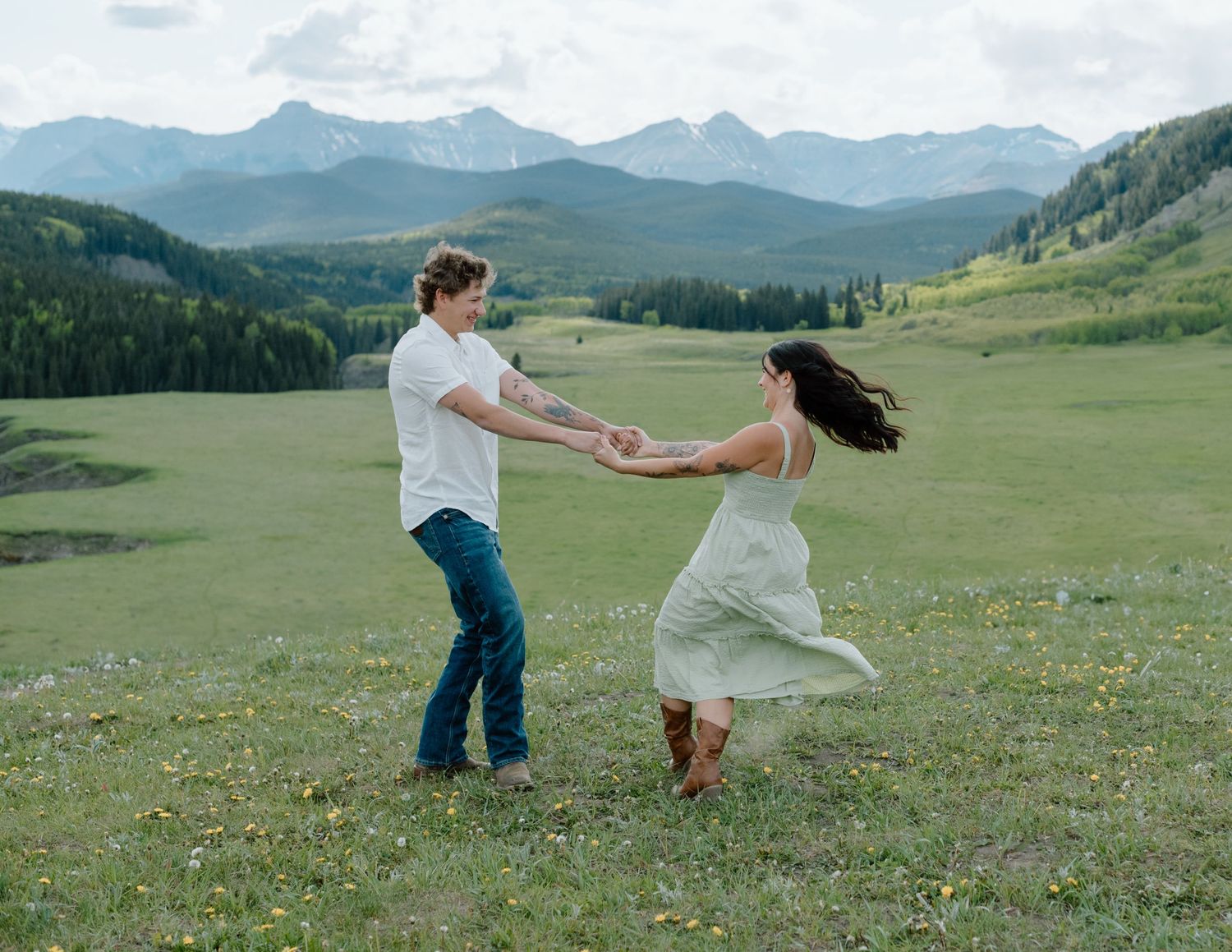 A couple dancing and spinning in a mountain field with wildflowers. Calgary Alberta Engagement Photographer.