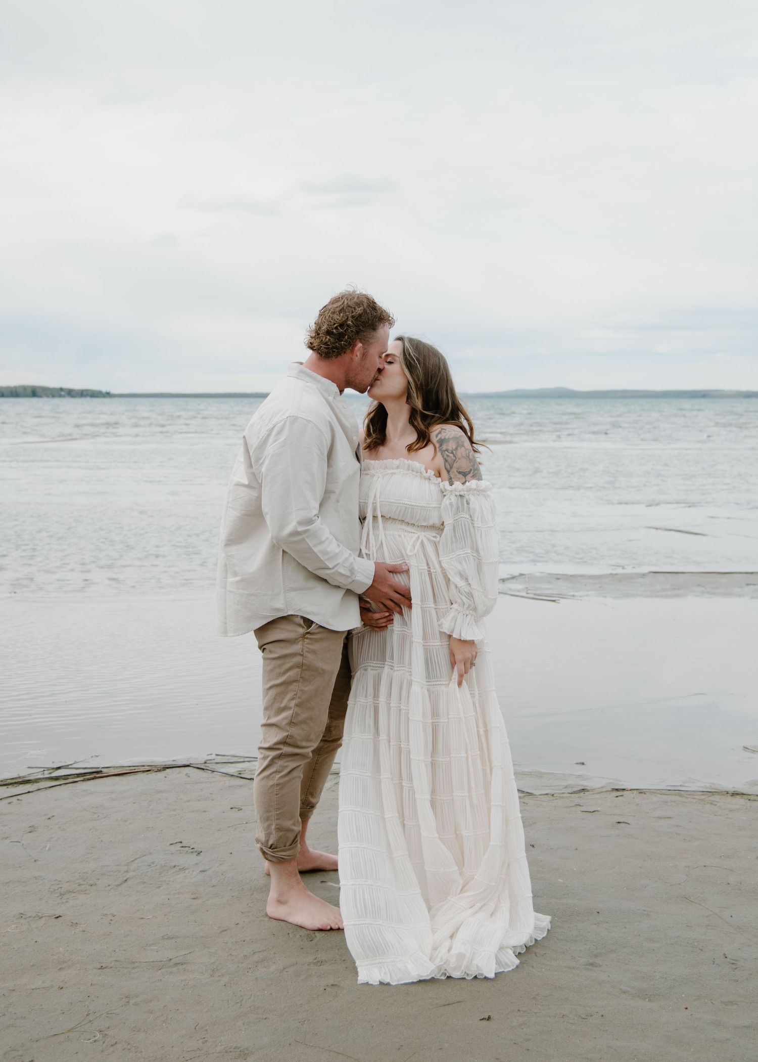 A romantic beachside maternity photo with a couple in neutral tones sharing an intimate moment. Calgary Alberta Maternity Photographer.