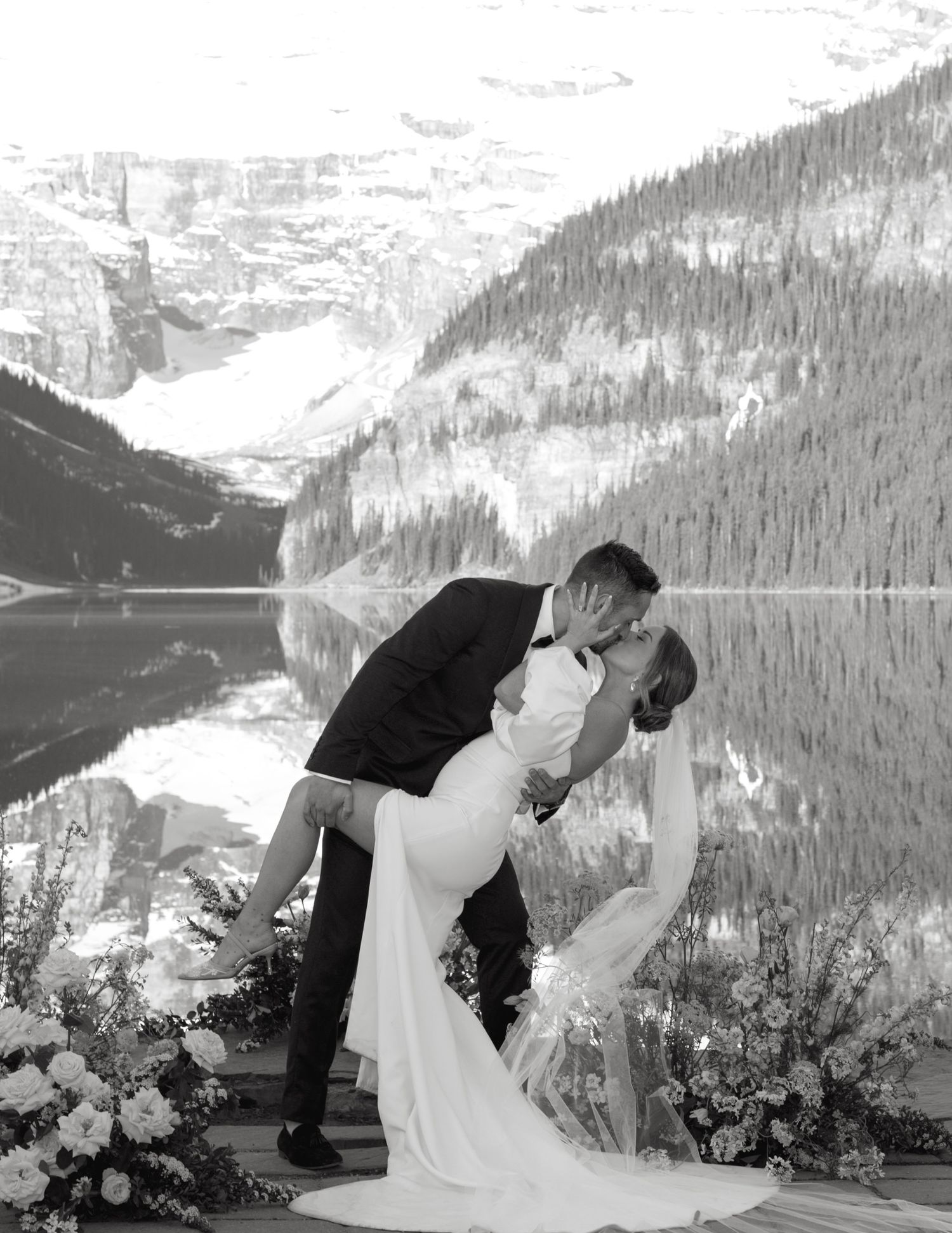 A romantic wedding couple shares a kiss with Lake Louise and the Canadian Rockies mountains as their backdrop.