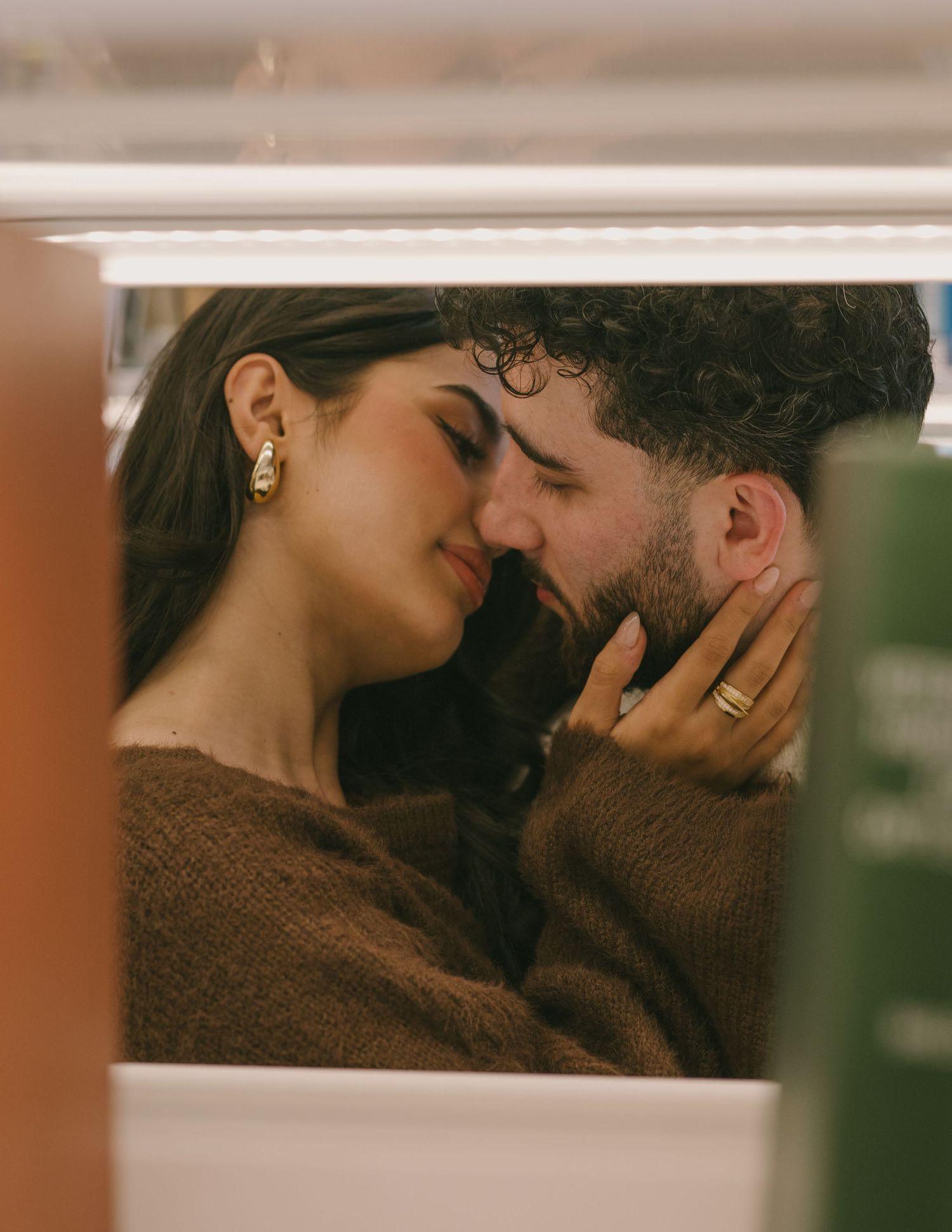 A romantic couple sharing an intimate moment in warm lighting with a brown sweater visible.