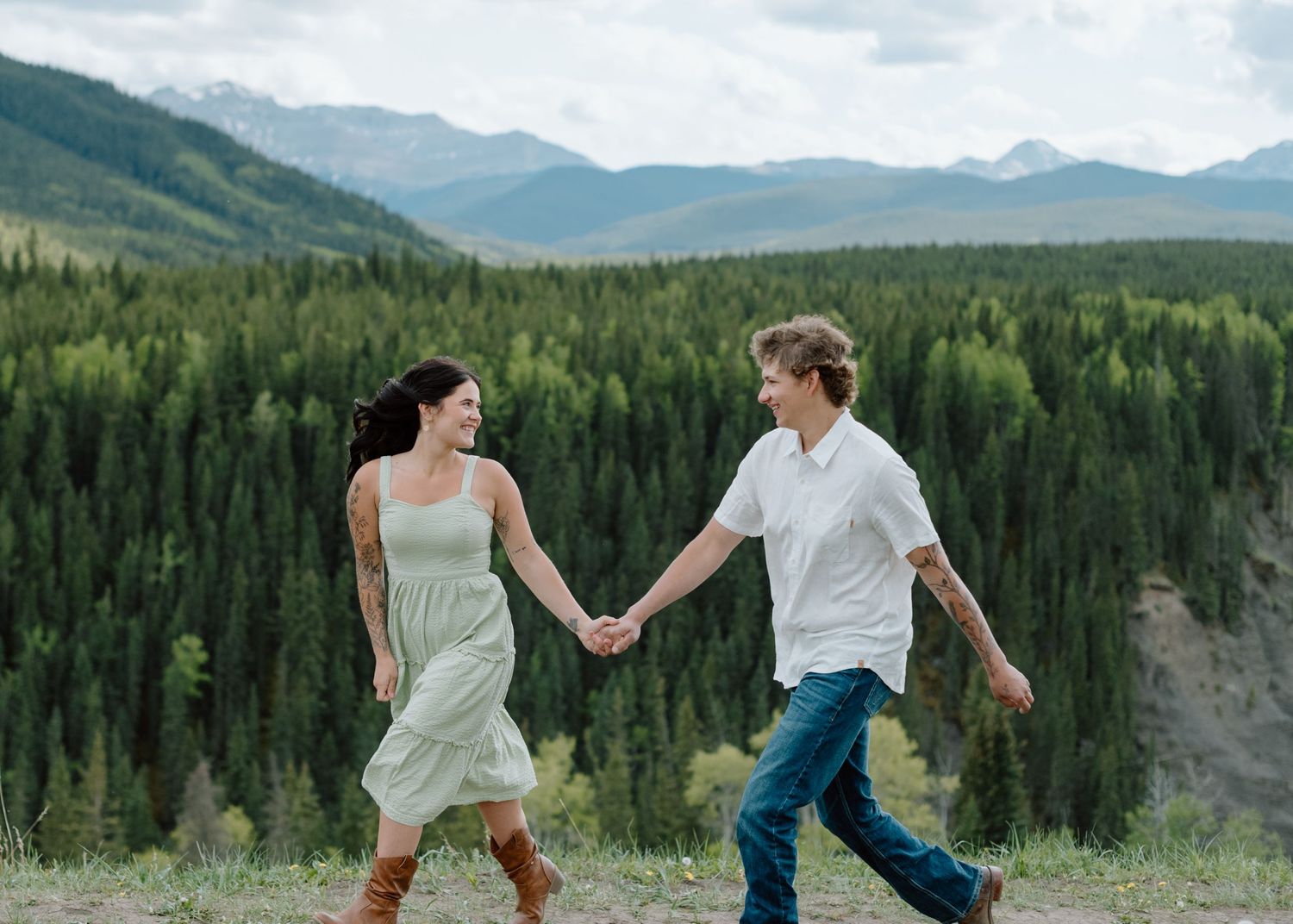 Two people holding hands and dancing in a mountain meadow. Calgary Alberta Engagement Photographer.