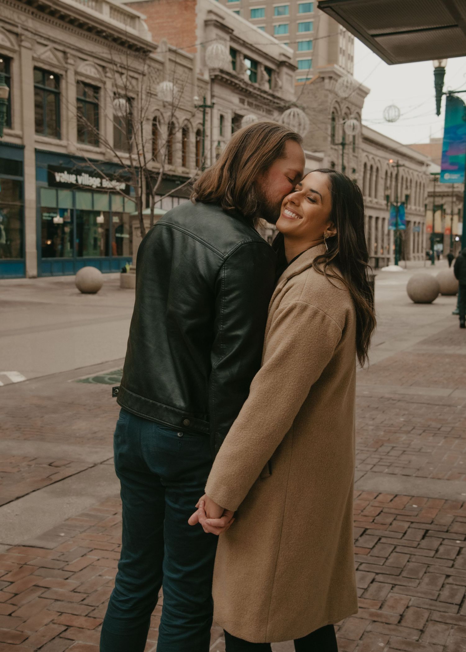 Couple laughing together on brick sidewalk in downtown setting. Calgary Alberta Engagement Photographer.