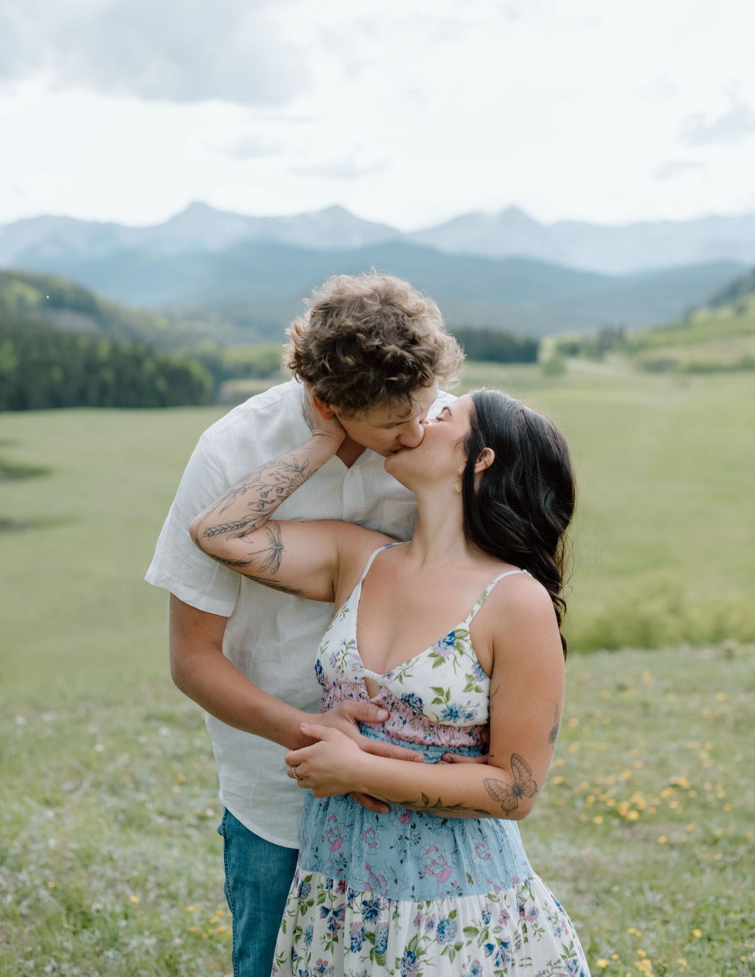 A loving couple sharing a close moment in a mountain field with wildflowers. Calgary Alberta Engagement Photographer.