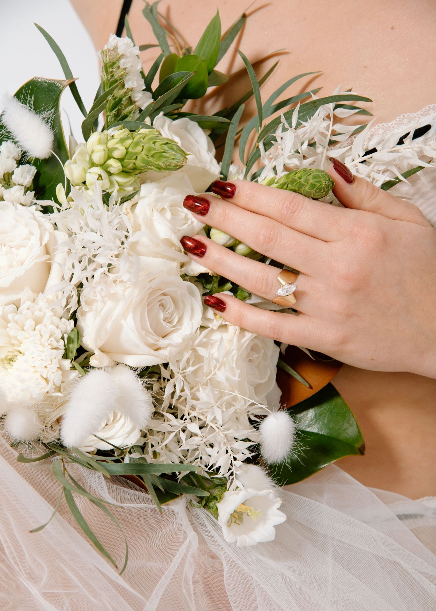 A hand with red nail polish touches a white rose wedding bouquet featuring delicate floral arrangements Calgary Bridal Boudoir Photographer