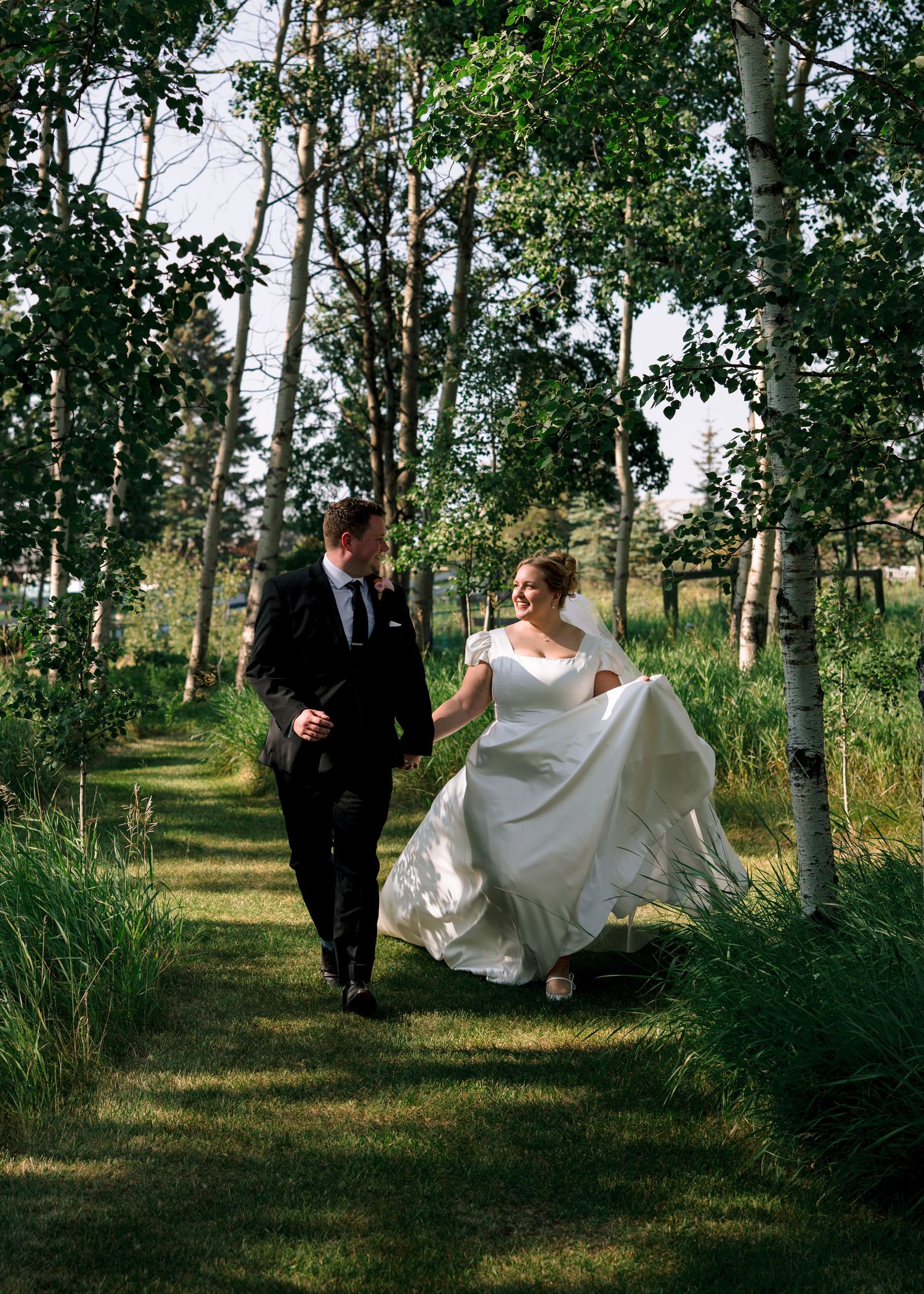 A couple walks hand in hand through a scenic aspen grove with sunlight streaming through the trees during their wedding.