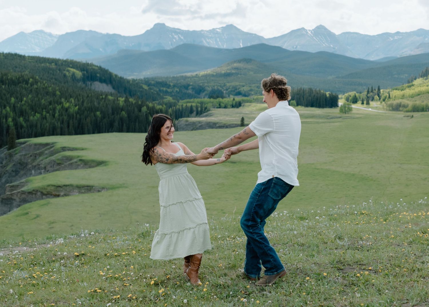 A couple dancing together on a grassy hillside with mountain peaks in the distance in Calgary, Alberta Calgary Lifestyle and Engagement