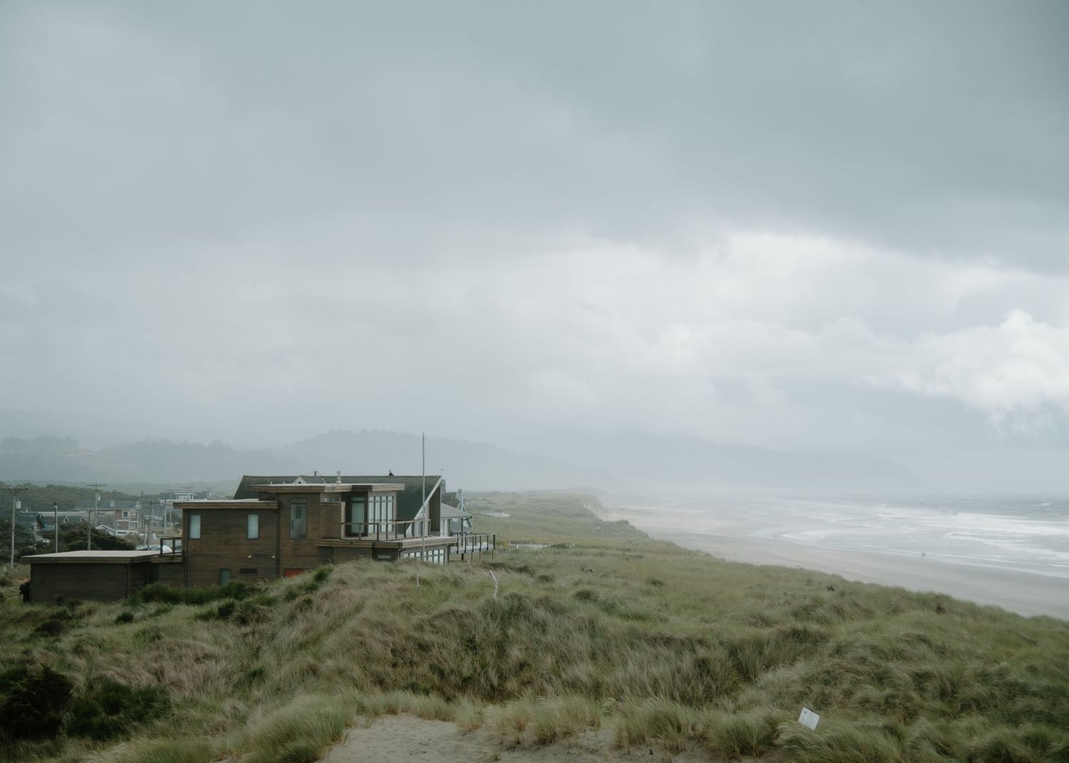 A rustic cabin perches on a cliff overlooking a misty coastal beach landscape on Oregon Coast. Calgary Lifestyle and Engagement Photographer